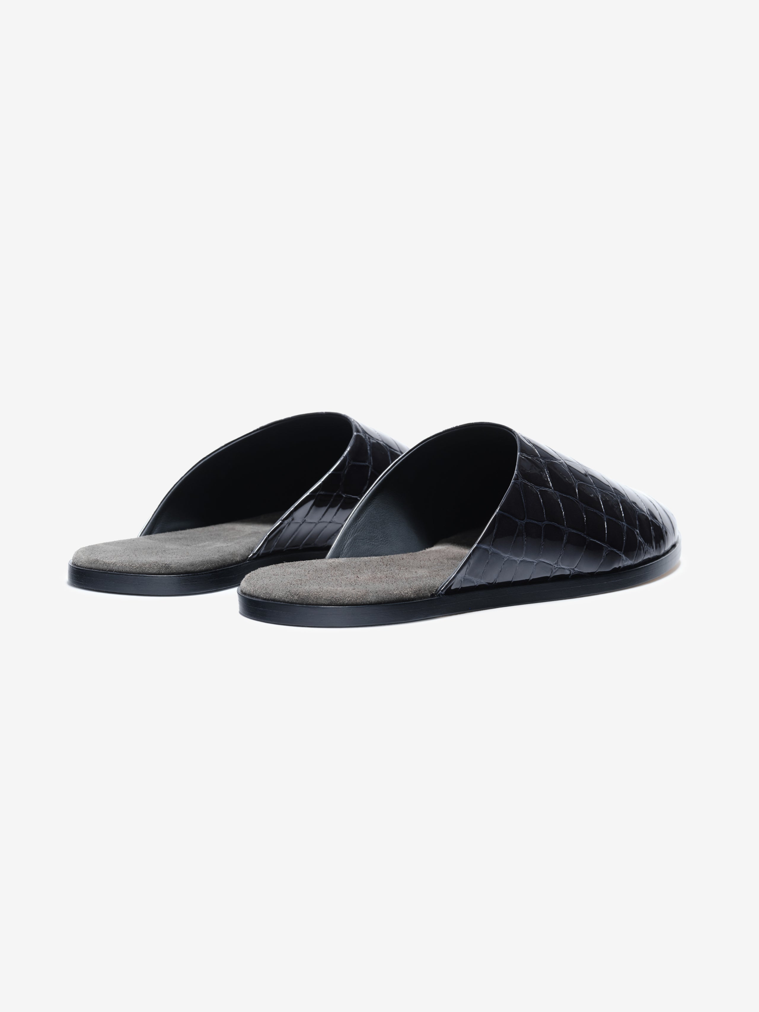Pair of black slip-on slippers with crocodile-embossed glossy upper and soft gray insoles on a white background