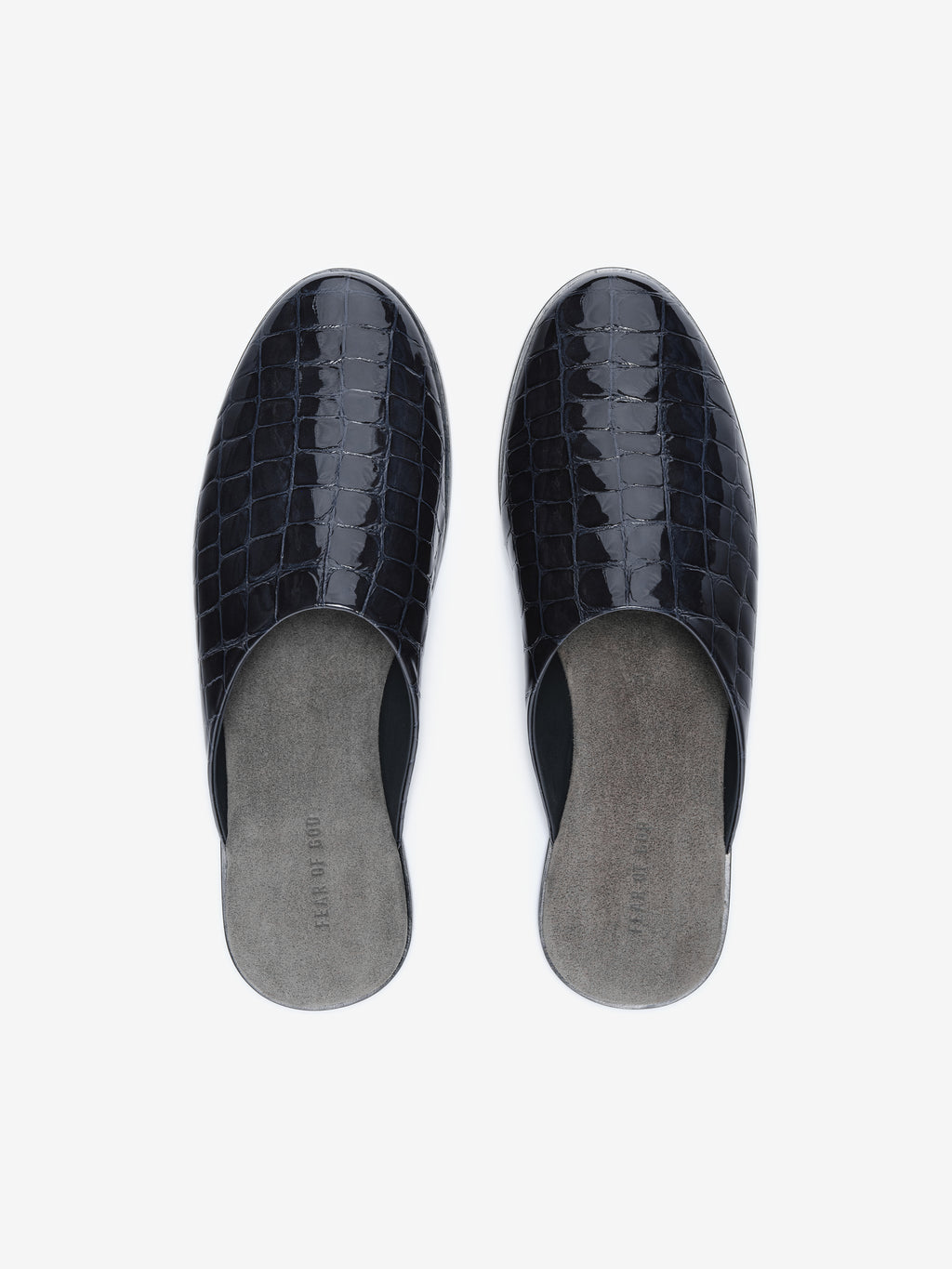 Top view of black glossy slip-on mules with crocodile texture and gray suede insoles on white background