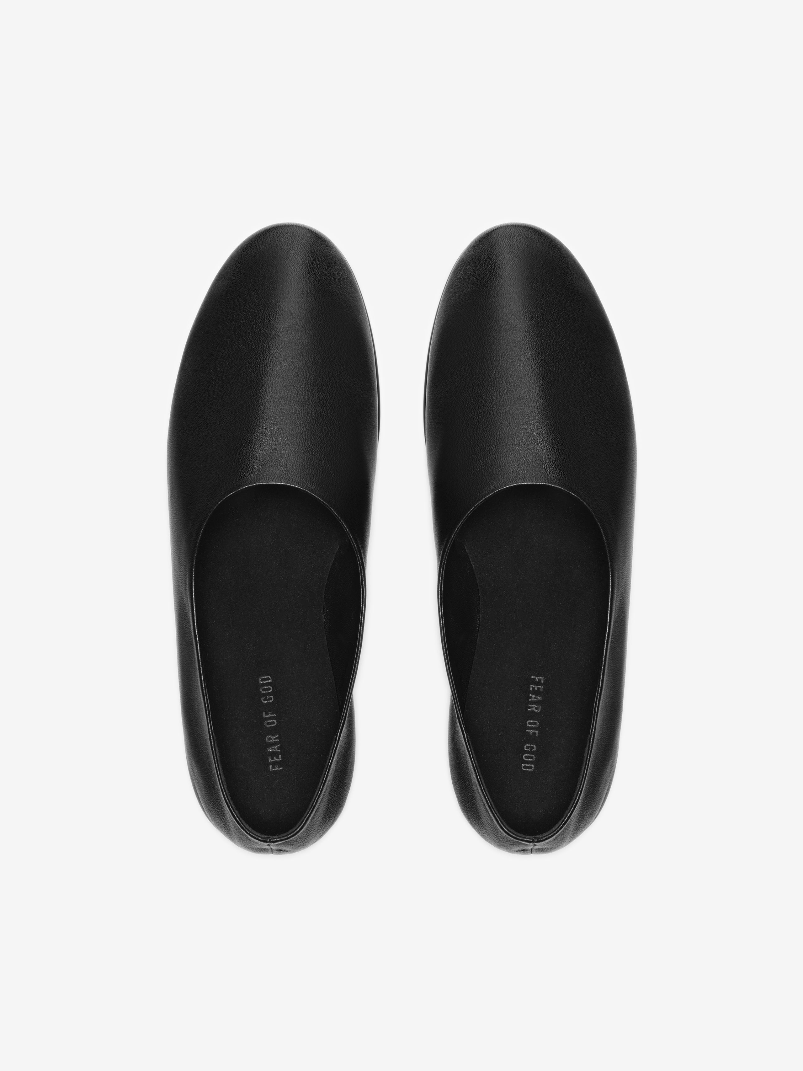 Top view of smooth black leather slip-on shoes with rounded toes and minimal design on light gray background