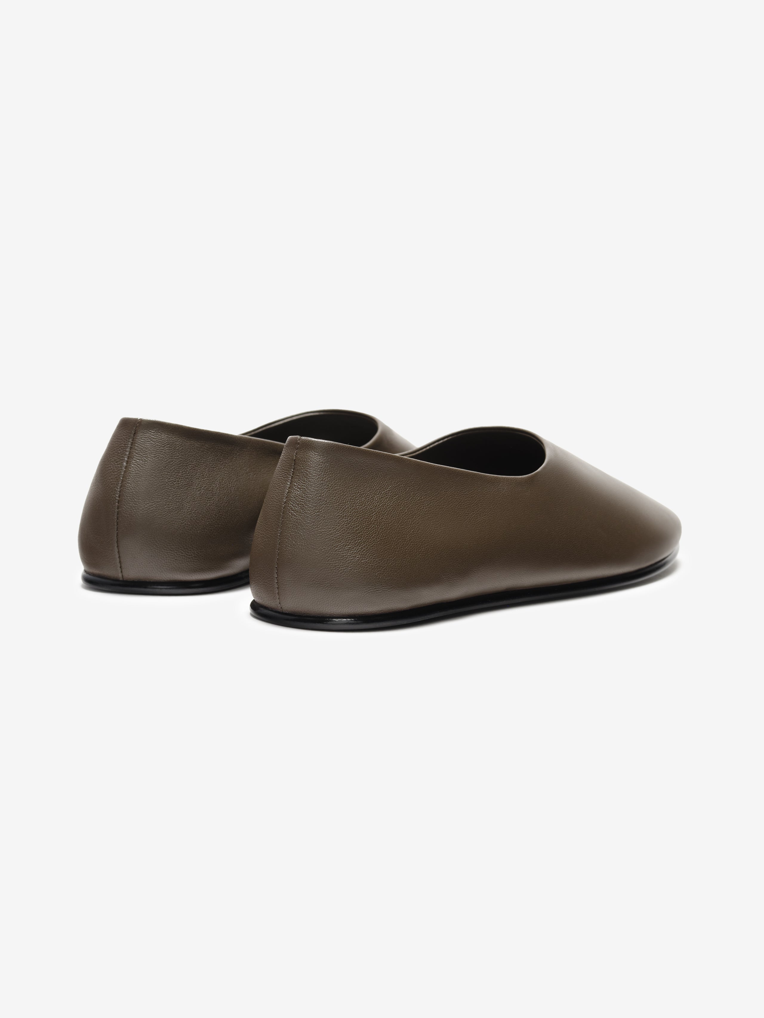 Pair of minimalist matte brown leather slip-on flats with rounded toes and low black soles on white background