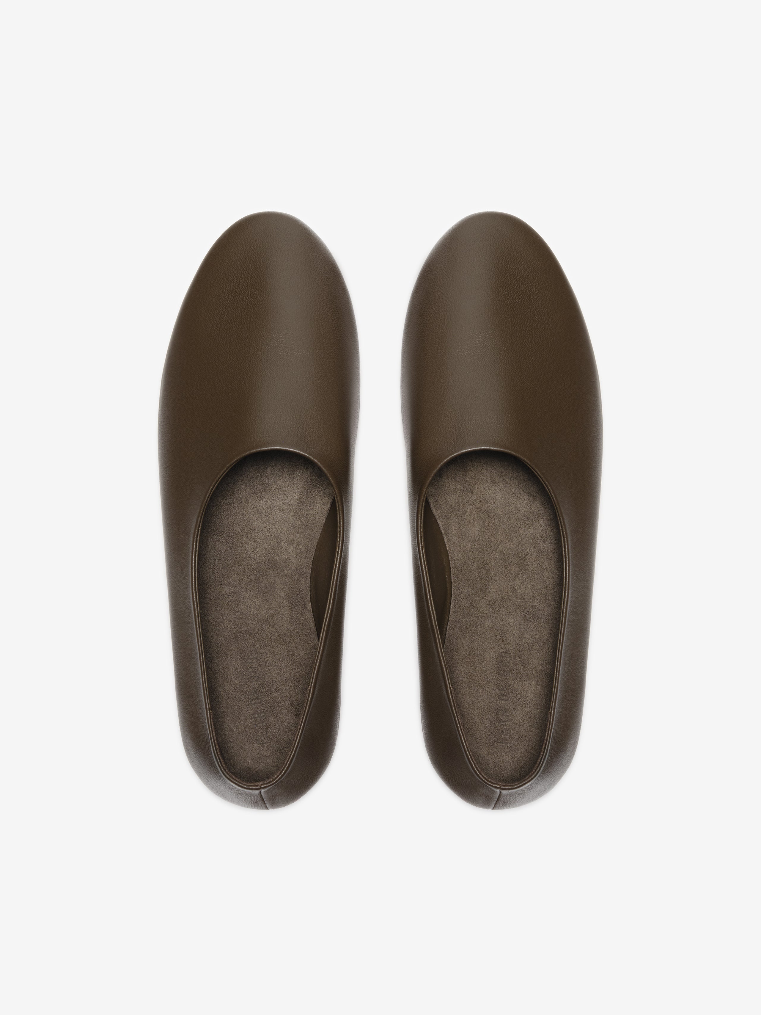 Overhead view of smooth dark brown leather slip-on flats with rounded toes and soft insoles on light background
