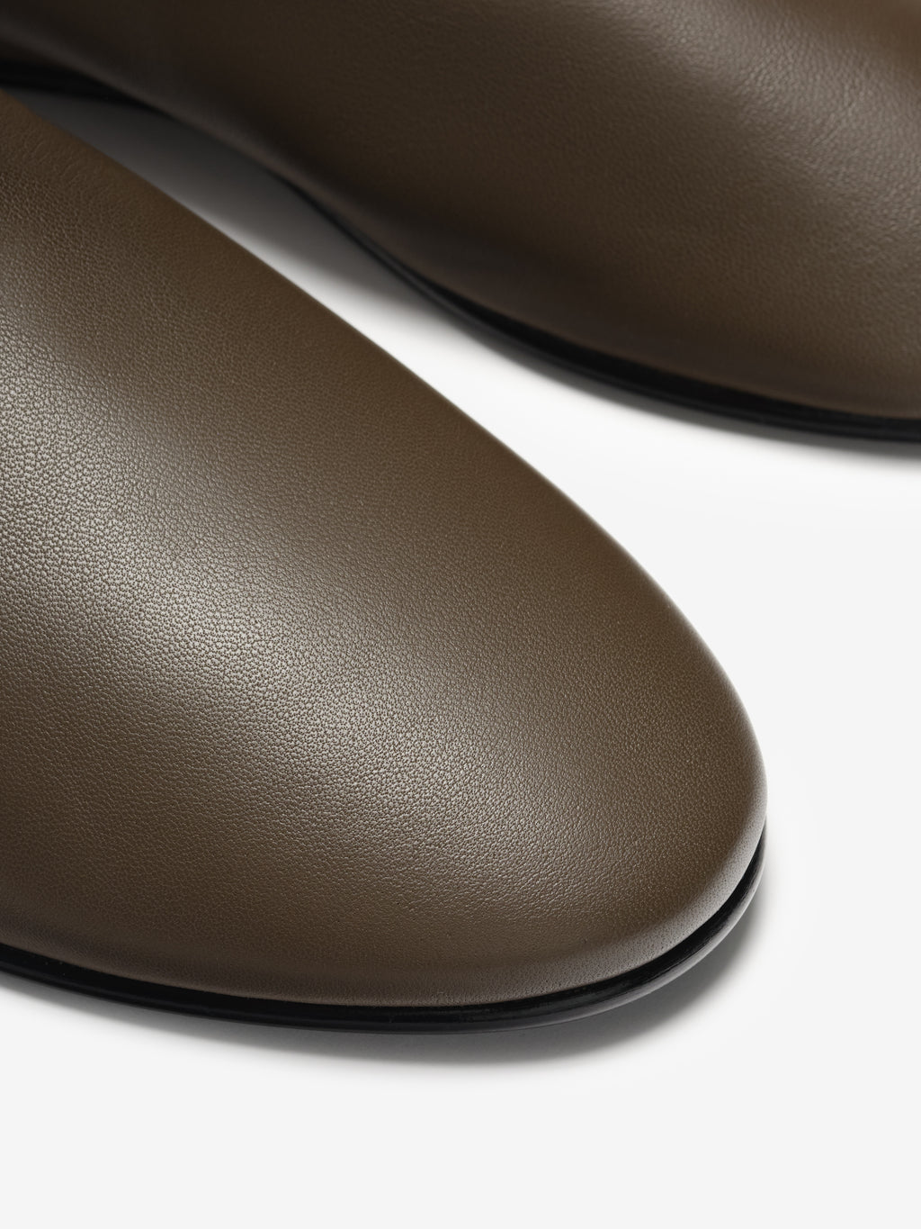 Close-up of smooth olive-brown leather shoes with rounded toes and black trim on a white background