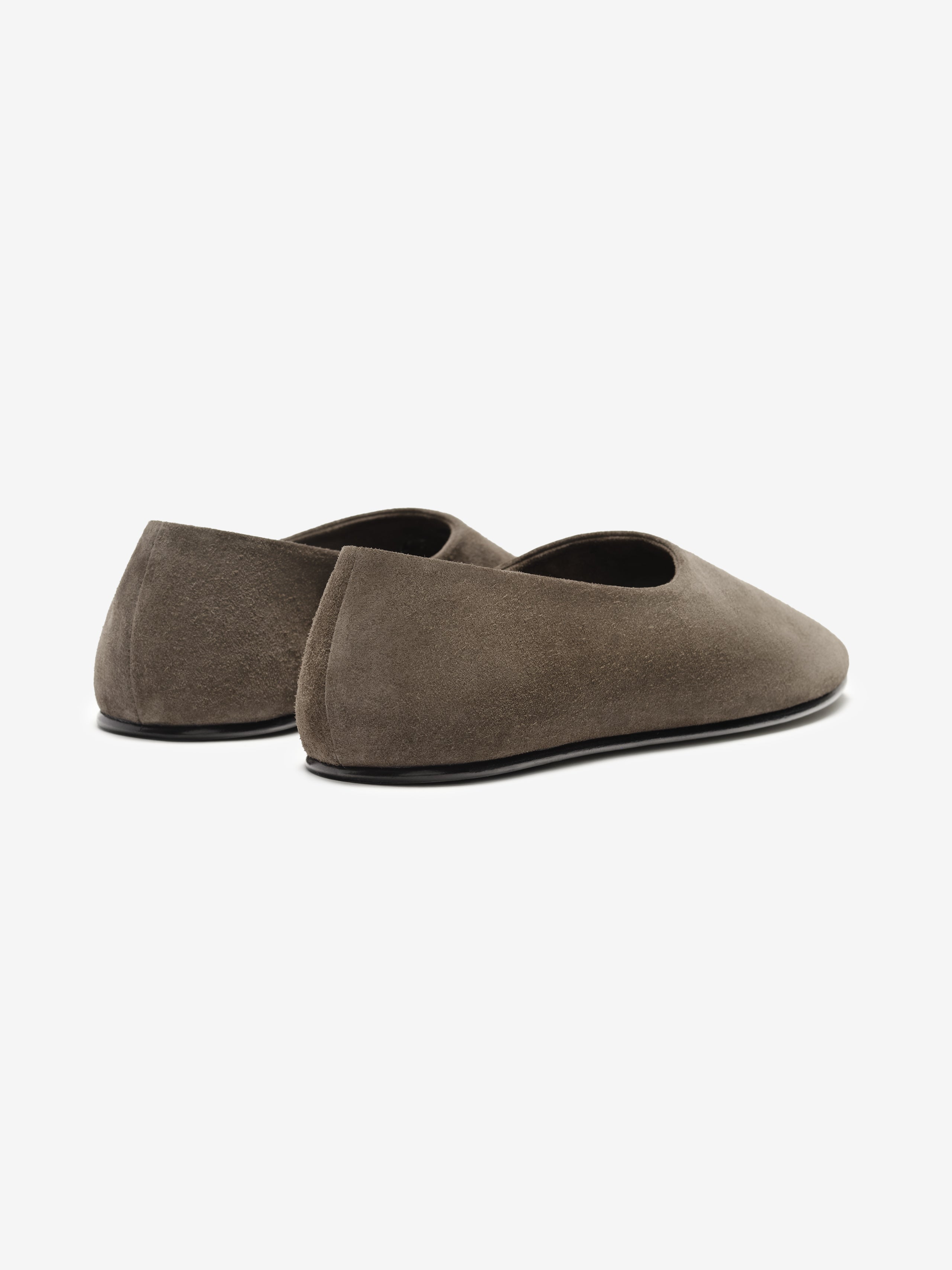 Pair of taupe suede ballet flats with rounded toe and slim black sole shown from rear angle on white background