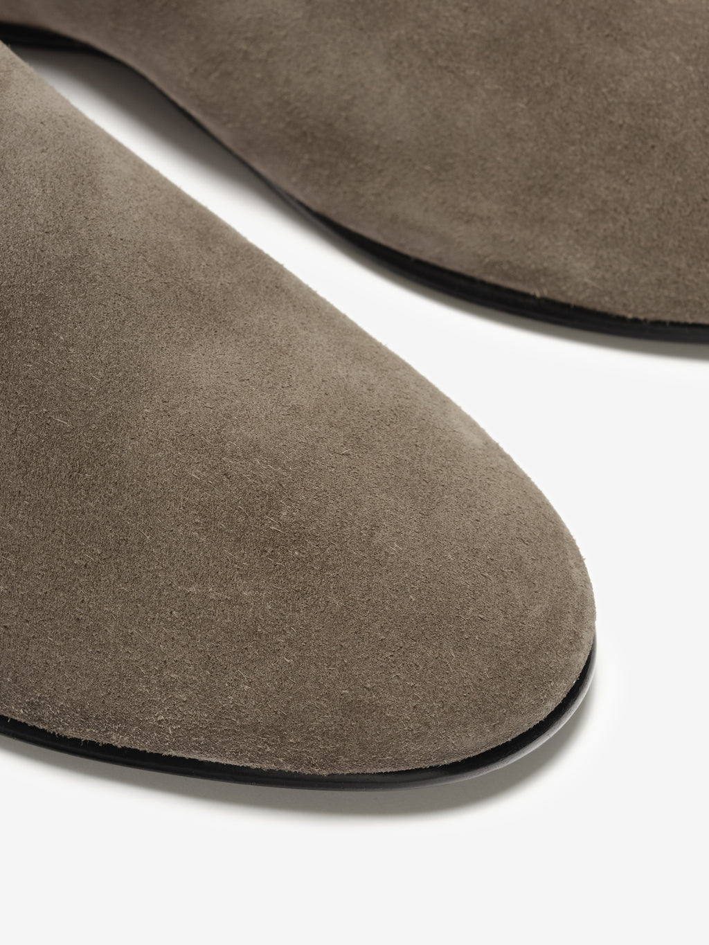 Close-up of taupe suede flats showing rounded toes and slim black soles on a white background