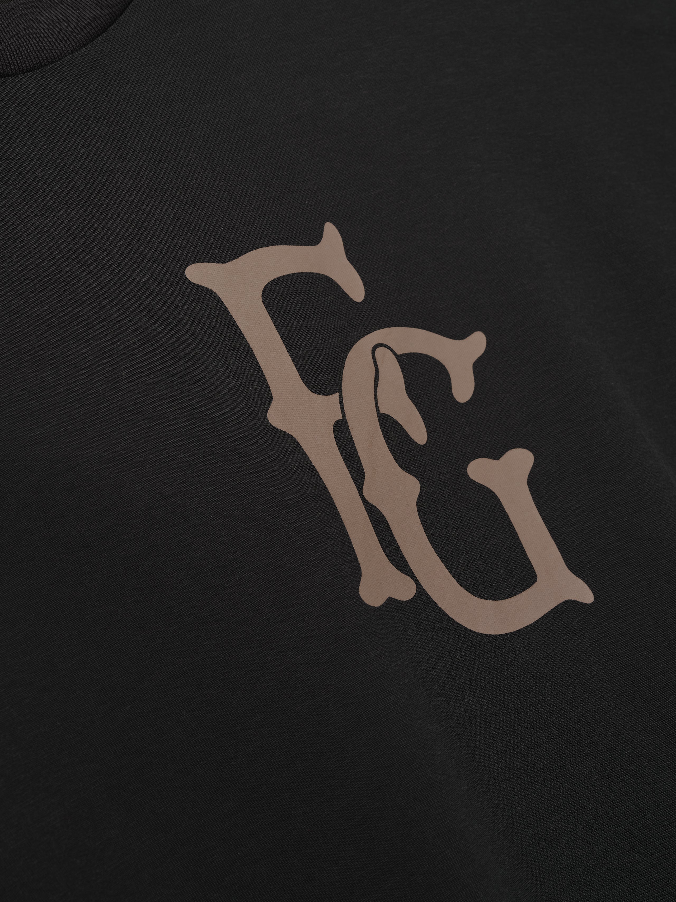 close-up of black cotton-rayon tee featuring large taupe vintage-style FG logo printed on chest