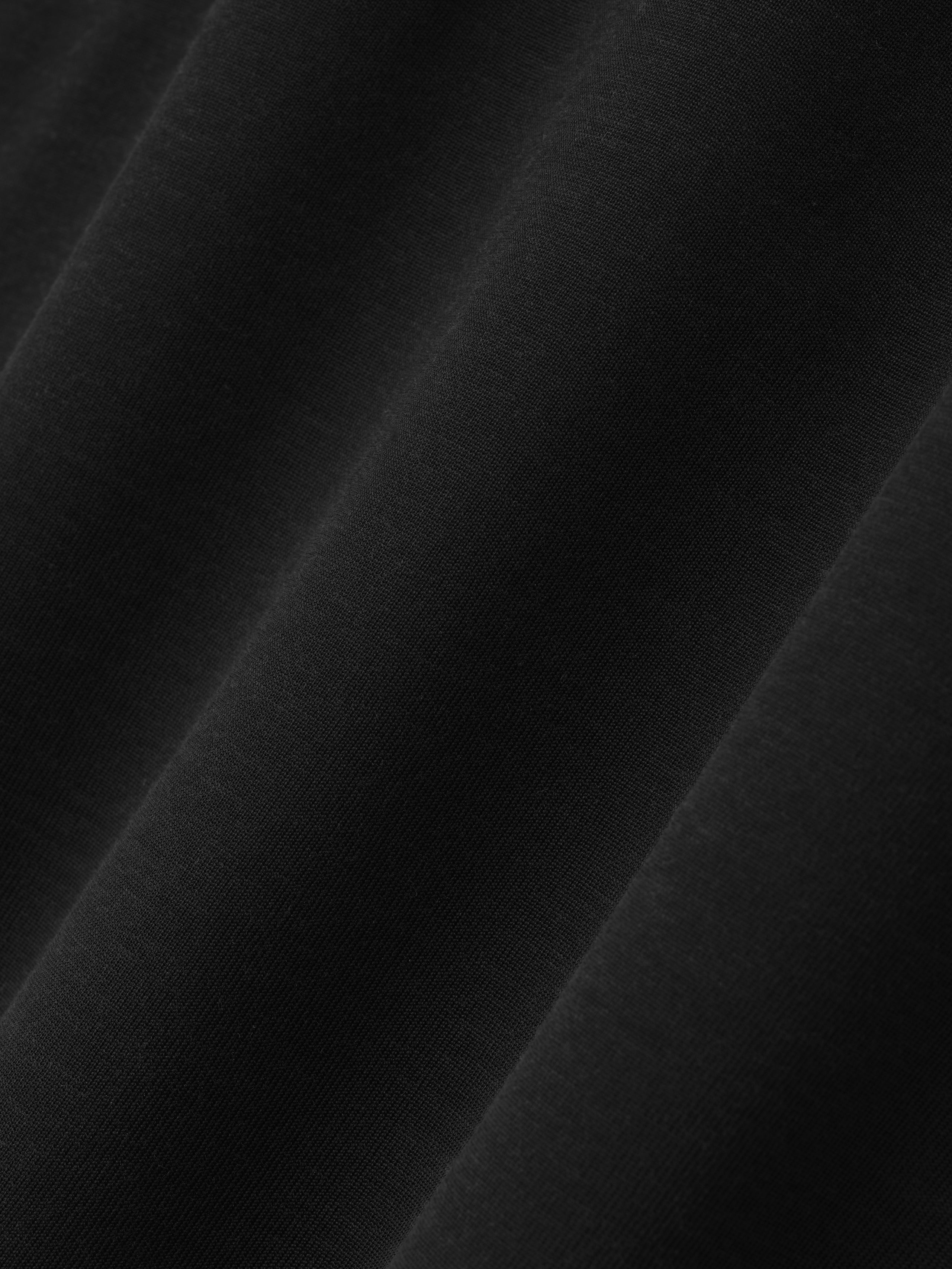 close-up of smooth black cotton-rayon fabric with subtle texture showing relaxed drape and soft garment wash finish