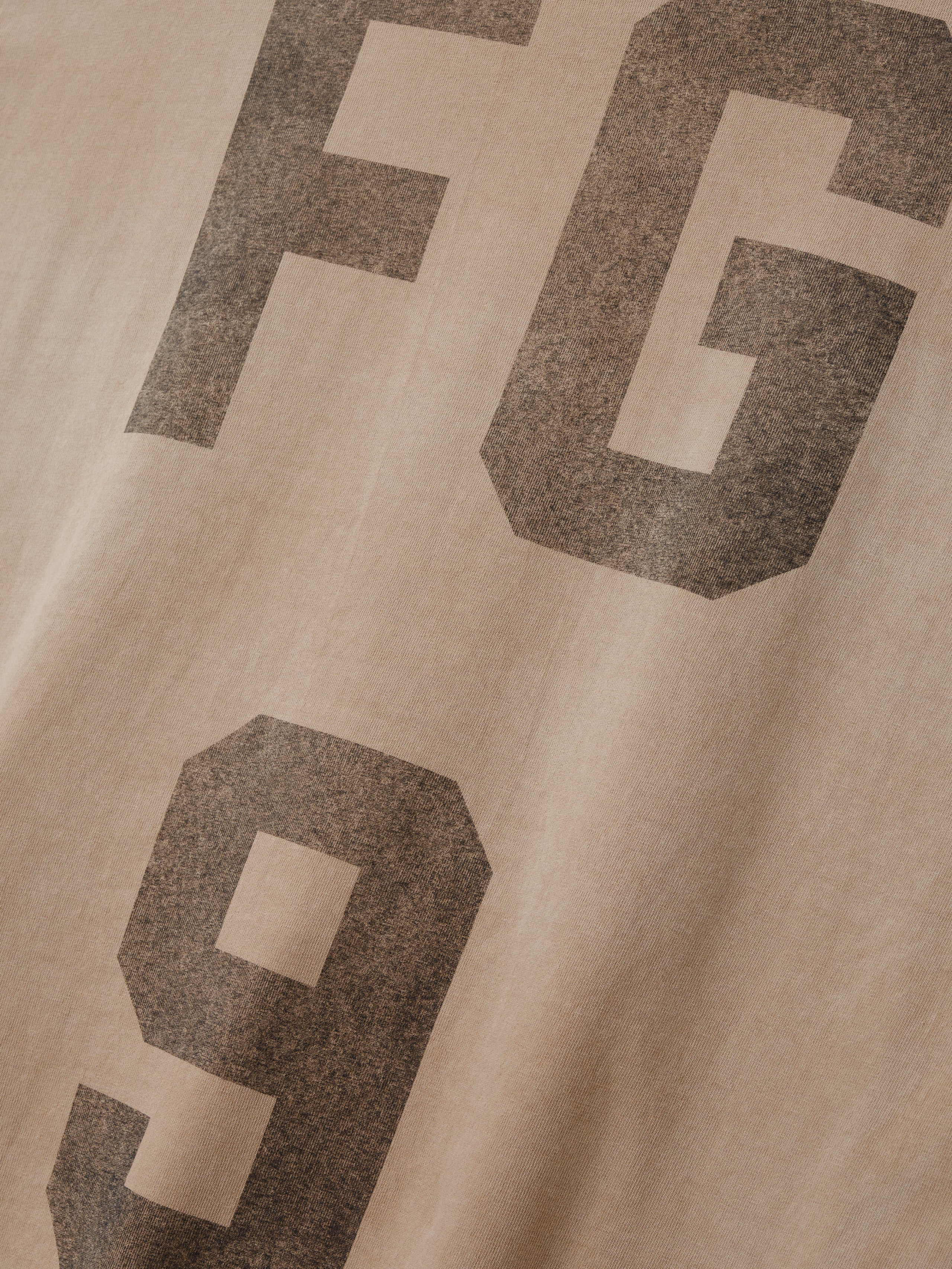close-up of faded beige cotton jersey fabric with large distressed "FG 9" print in dark gray