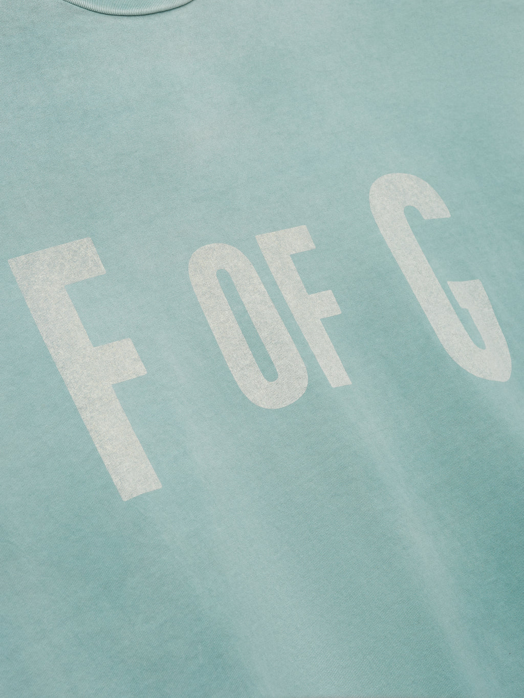 Close-up of a soft sky blue fabric with large faded white letters "F OF G" printed on the front