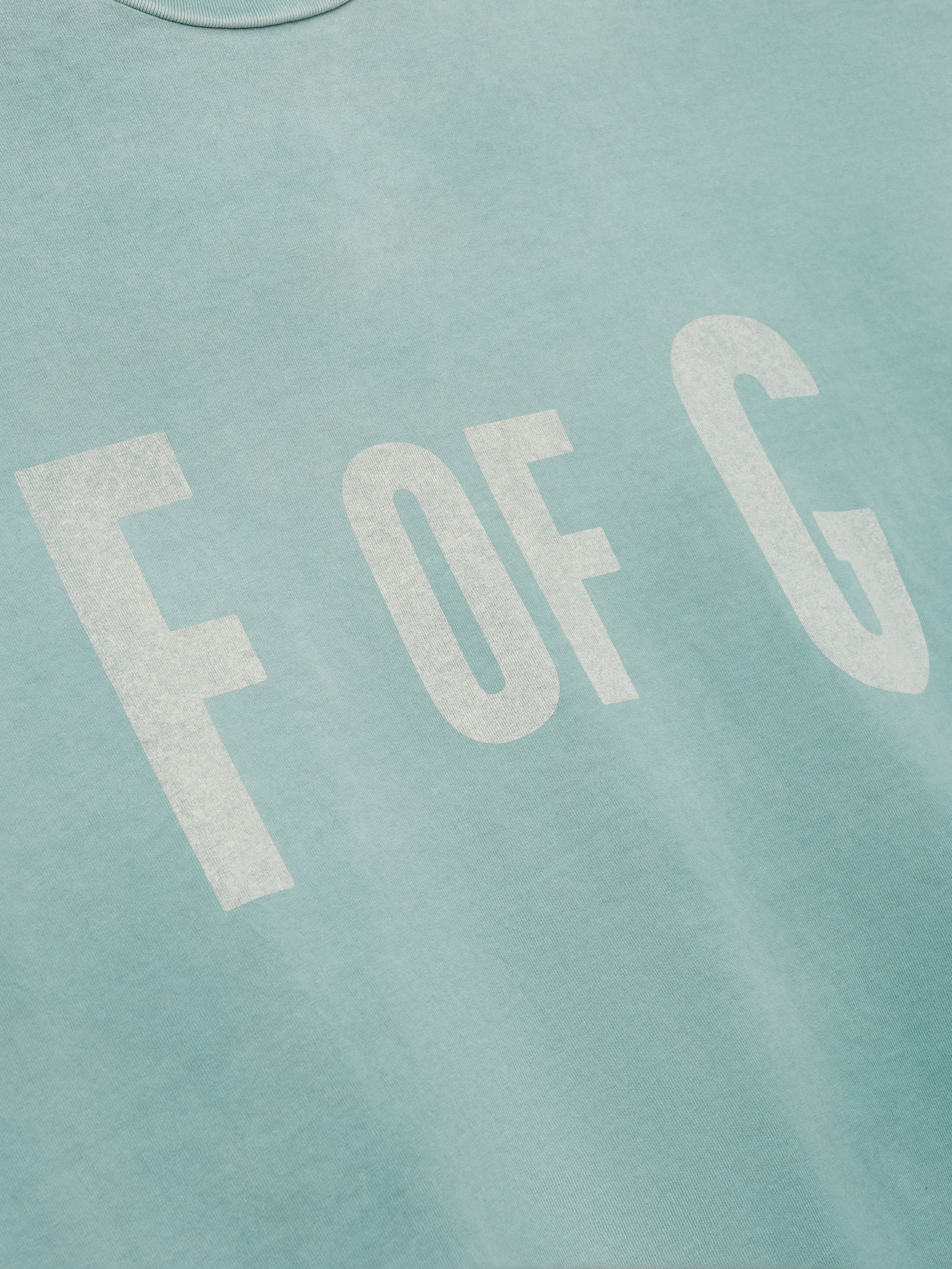 Close-up of a soft sky blue fabric with large faded white letters "F OF G" printed on the front
