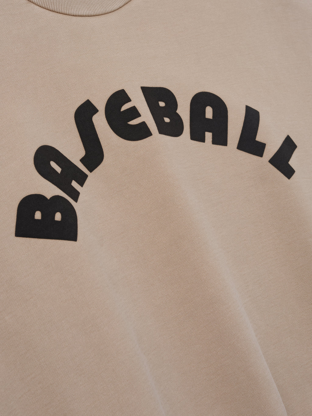 Close-up of soft dune-colored fabric with large black arched "BASEBALL" text printed on front panel