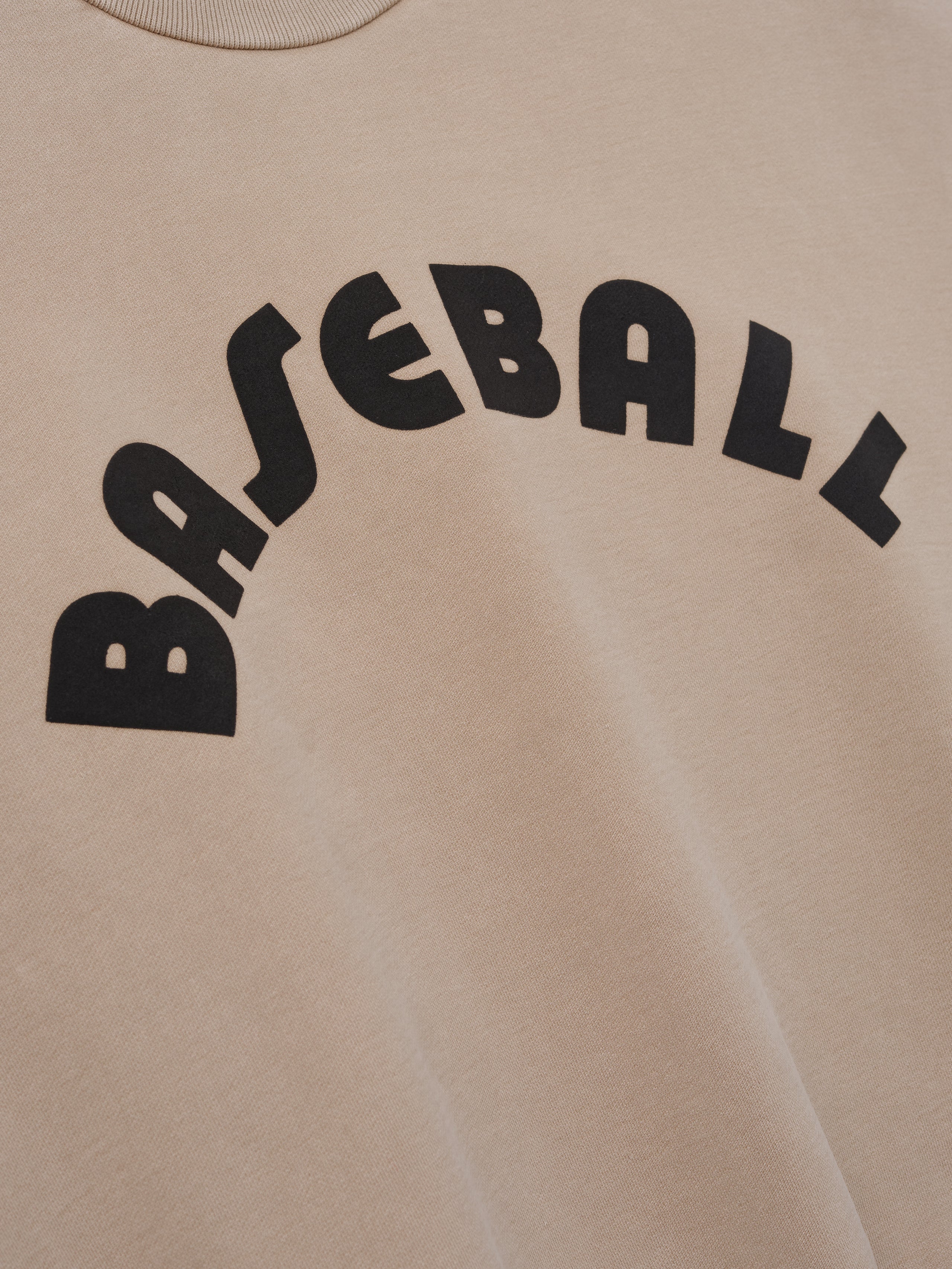Close-up of soft dune-colored fabric with large black arched "BASEBALL" text printed on front panel