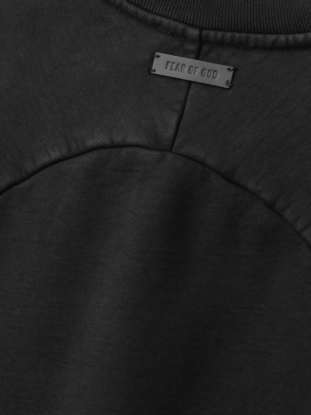 close-up of black heavyweight cotton fleece fabric with curved raglan seam and Fear of God logo patch on back neckline