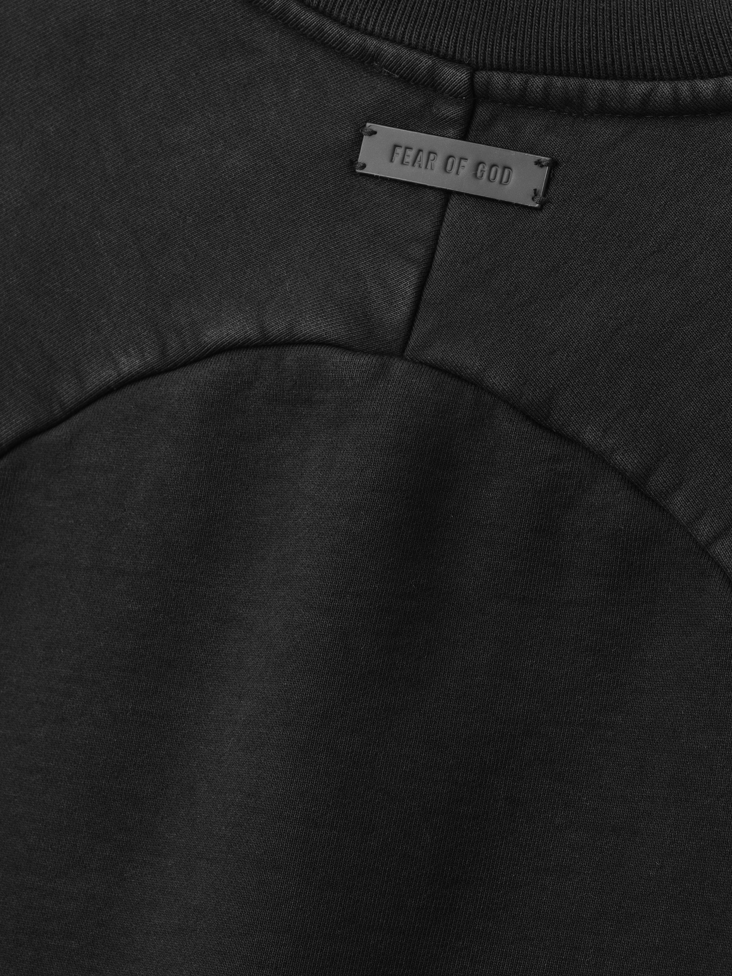 close-up of black heavyweight cotton fleece fabric with curved raglan seam and Fear of God logo patch on back neckline