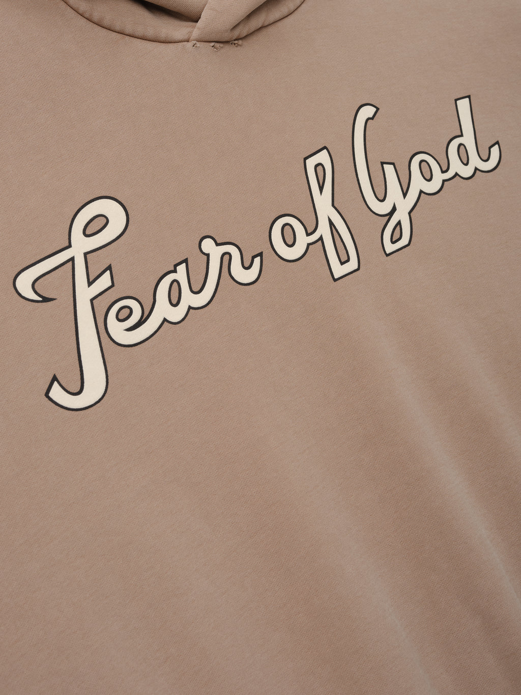 Close-up of a dune-colored hoodie with cream "Fear of God" cursive script printed diagonally across the chest