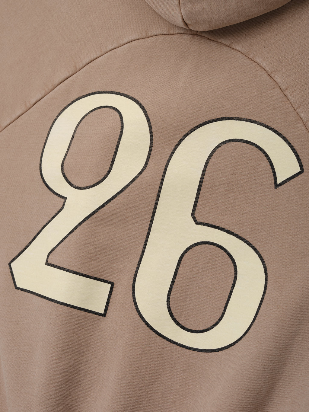 Close-up of a dune-colored hoodie back with large cream number 26 outlined in black printed on fabric