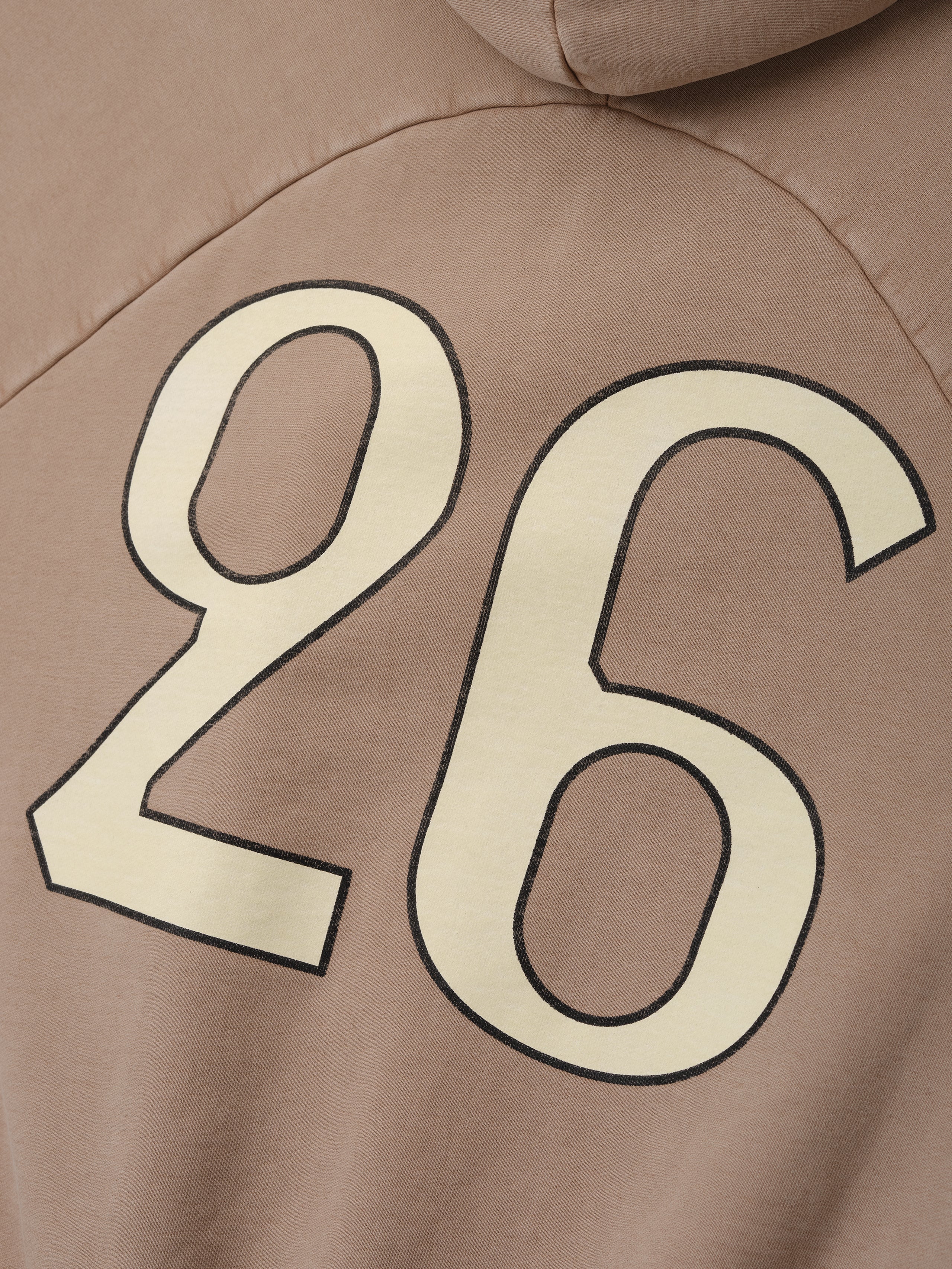 Close-up of a dune-colored hoodie back with large cream number 26 outlined in black printed on fabric