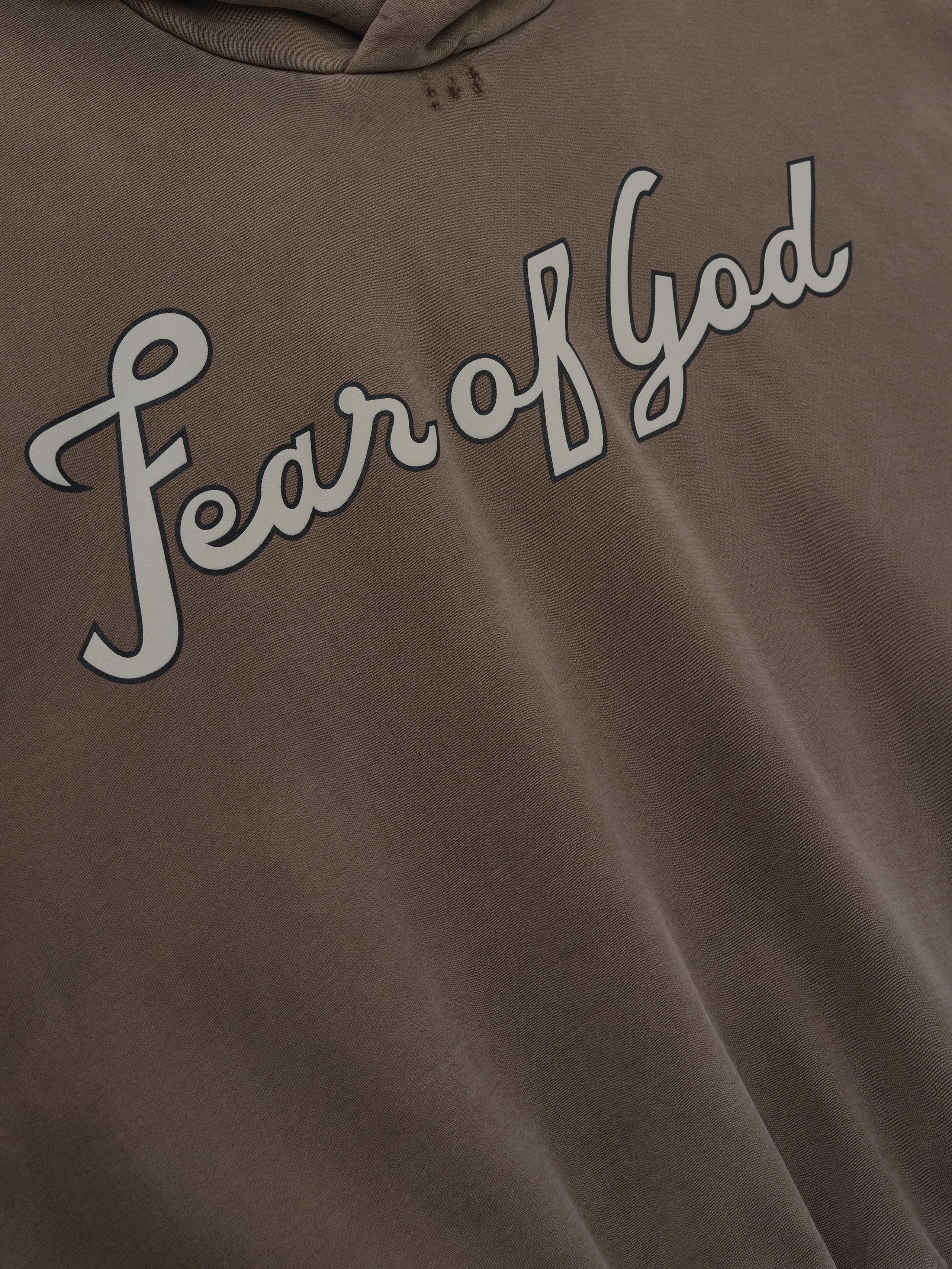 close-up of garment-washed heavyweight cotton fleece hoodie with hand-painted "Fear of God" script on chest