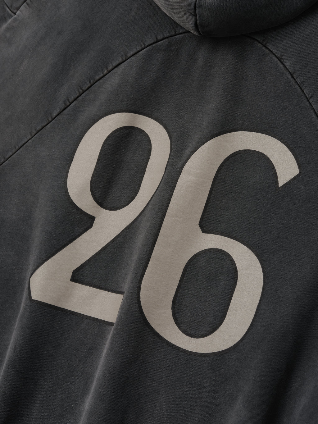 Close-up of off-black cotton fabric with large beige "26" printed on the back of a hoodie with hood visible
