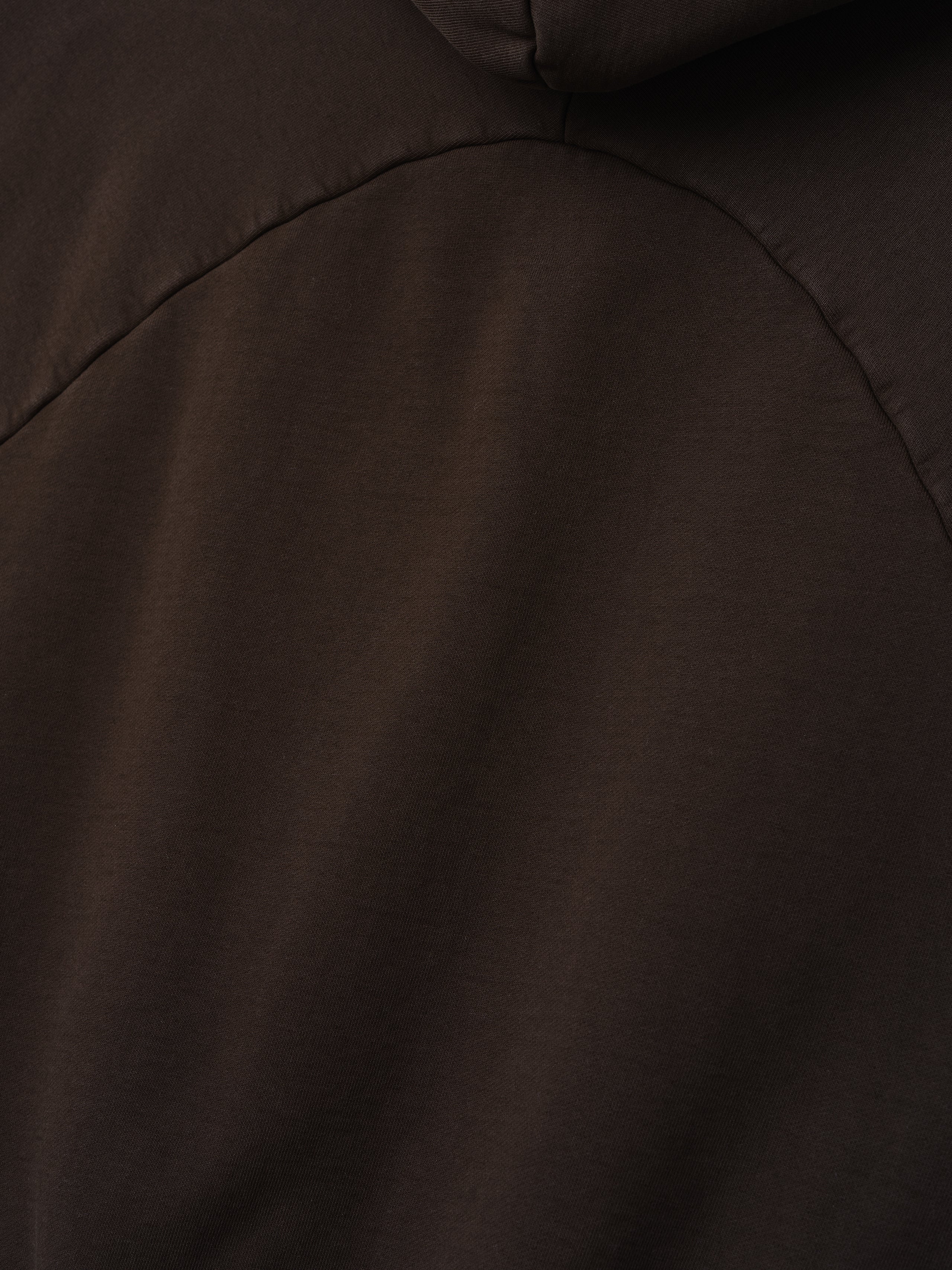 close-up detail of dark brown heavyweight cotton fleece fabric with curved seam of half raglan sleeve hoodie