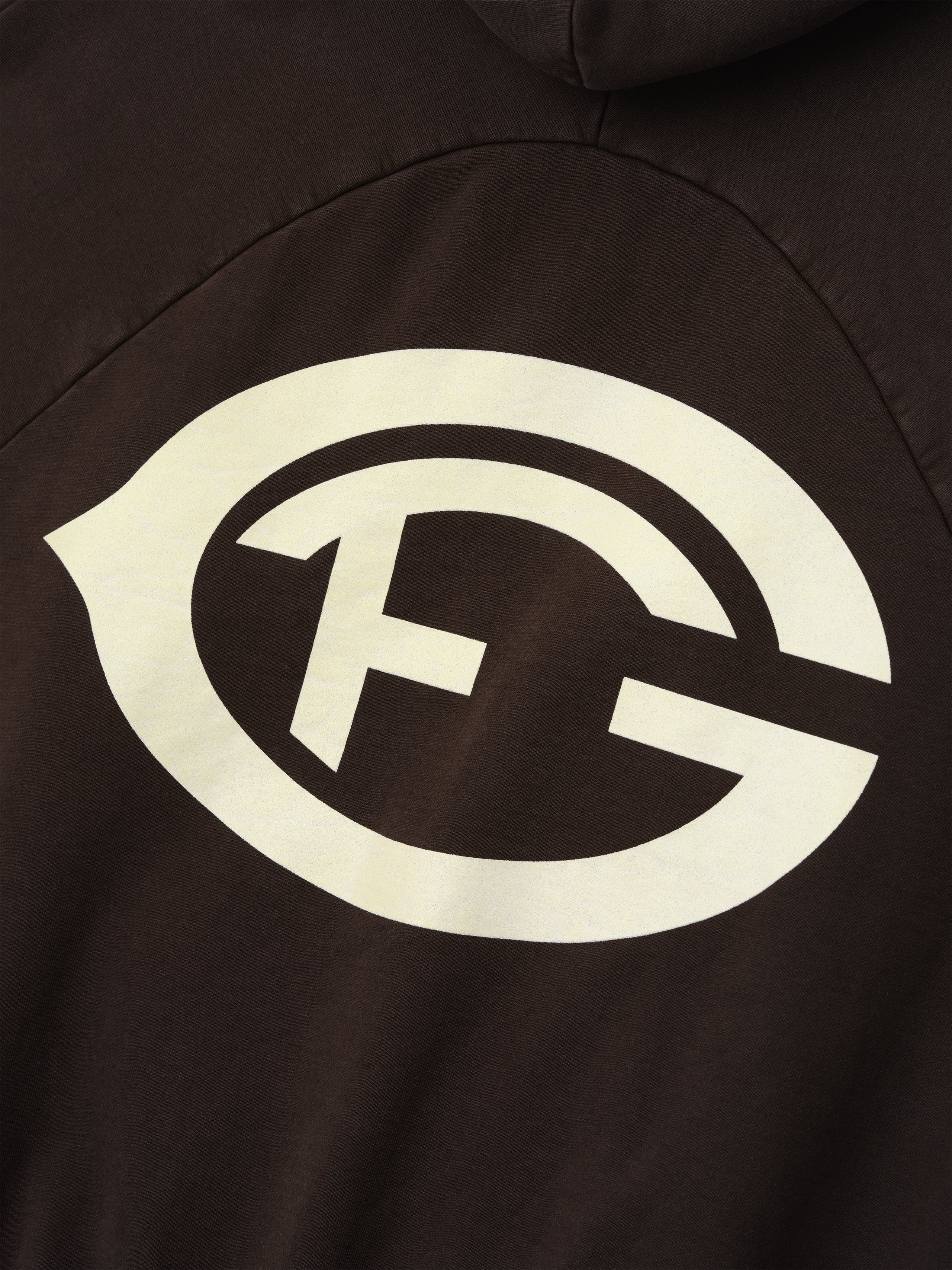 cream F of G logo graphic printed on dark brown heavyweight cotton fleece fabric of hoodie back