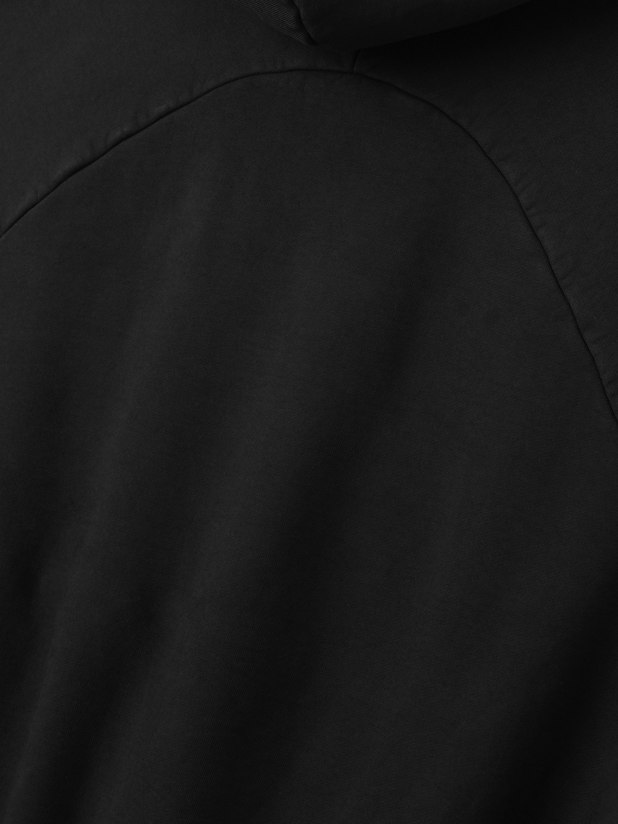close-up of black heavyweight cotton fleece fabric and curved seam detail of half raglan sleeve hoodie back