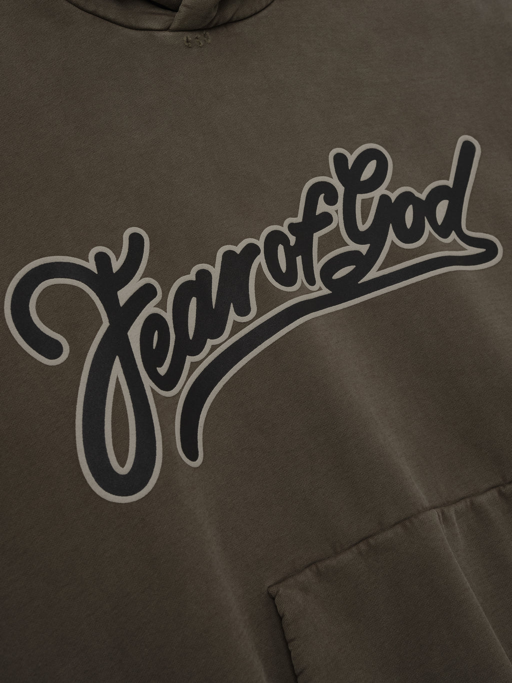 Close-up of faded brown hoodie with large dark gray cursive "Fear of God" text outlined in light gray above front pocket