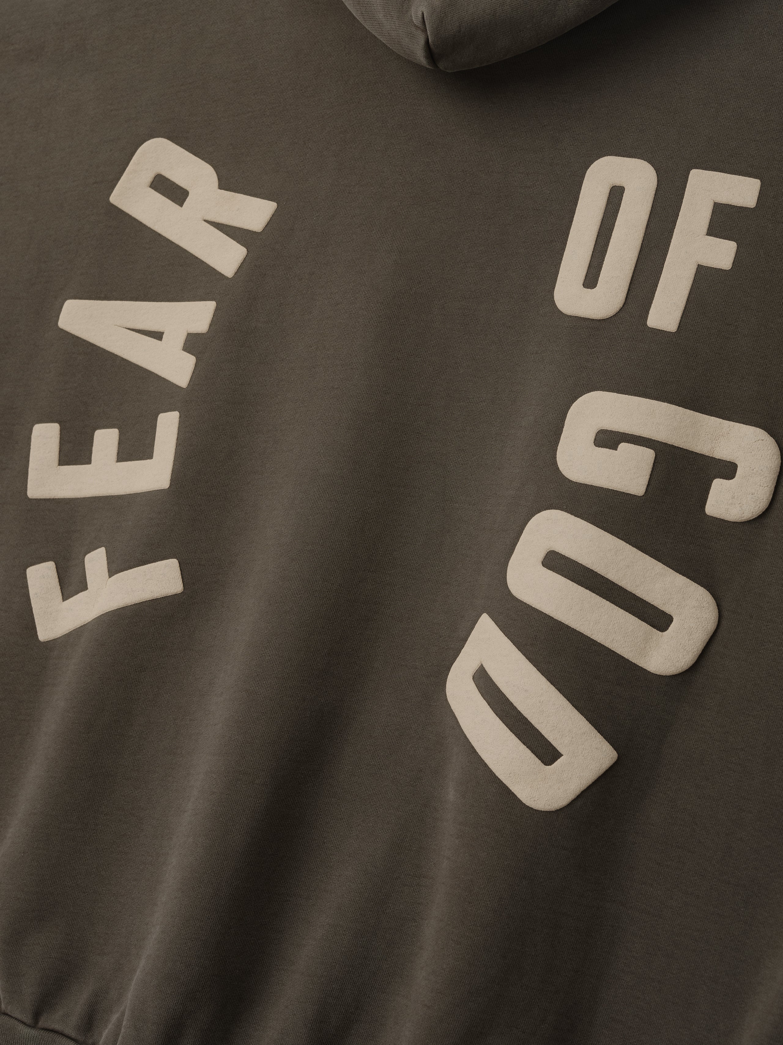 Close-up of faded brown fabric with beige block letters arranged diagonally spelling "FEAR OF GOD" on sweatshirt material
