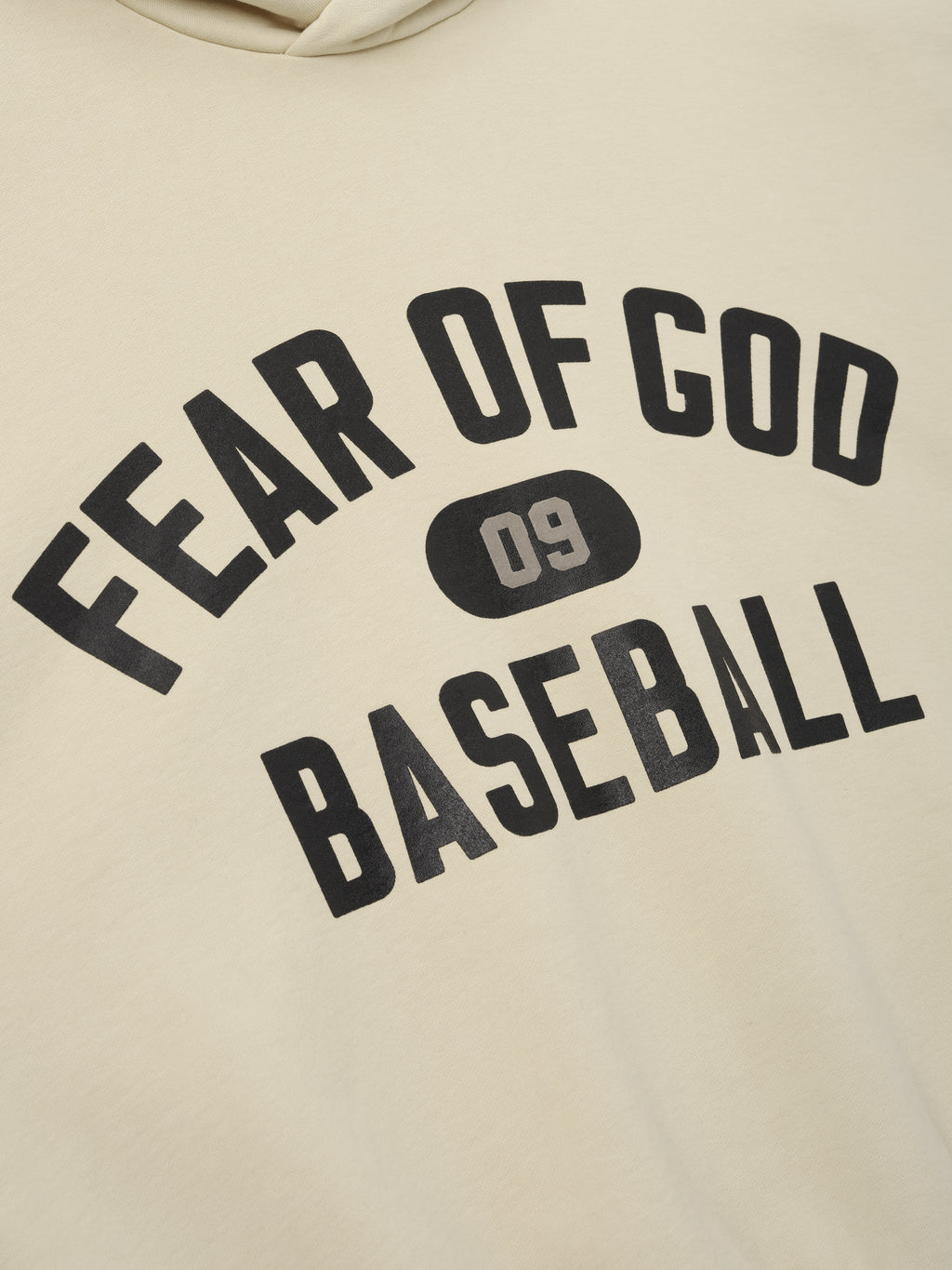 Close-up of off-white hoodie showing black "Fear of God Baseball" text and "09" emblem printed on the front fabric