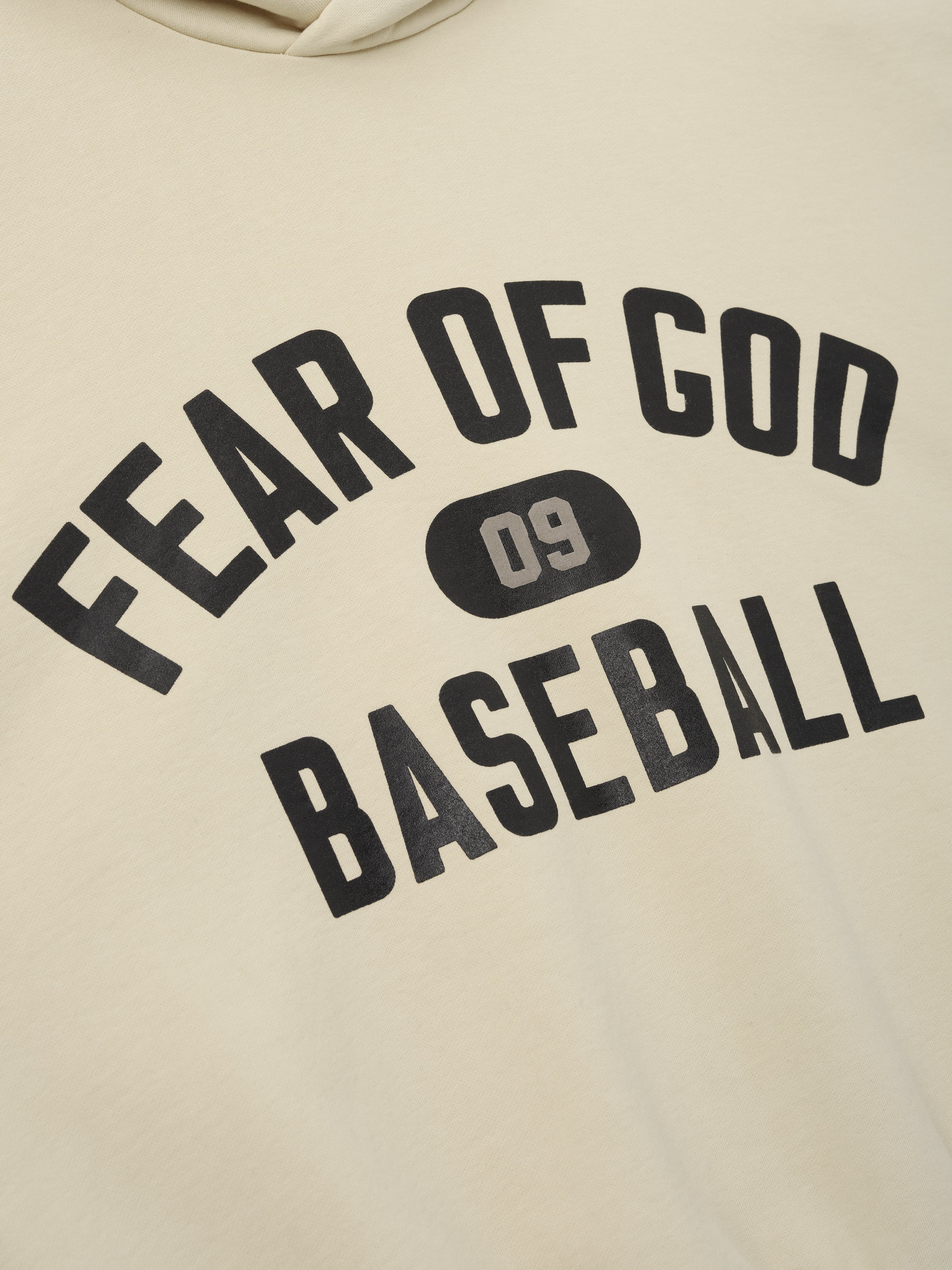 Close-up of off-white hoodie showing black "Fear of God Baseball" text and "09" emblem printed on the front fabric