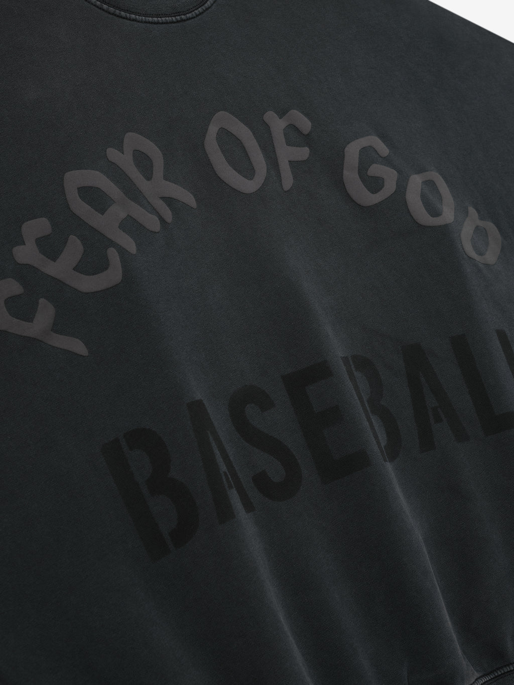 Close-up of black sweatshirt with glossy and matte "Fear of God Baseball" text printed in curved and block letters