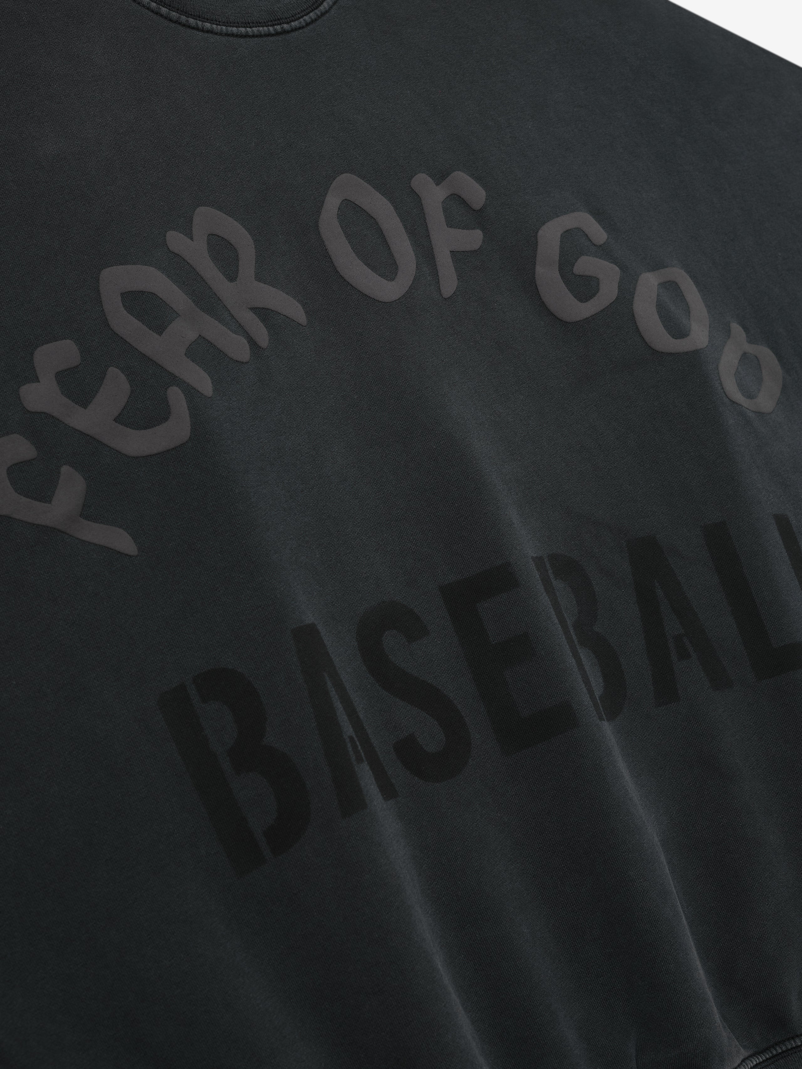 Close-up of black sweatshirt with glossy and matte "Fear of God Baseball" text printed in curved and block letters
