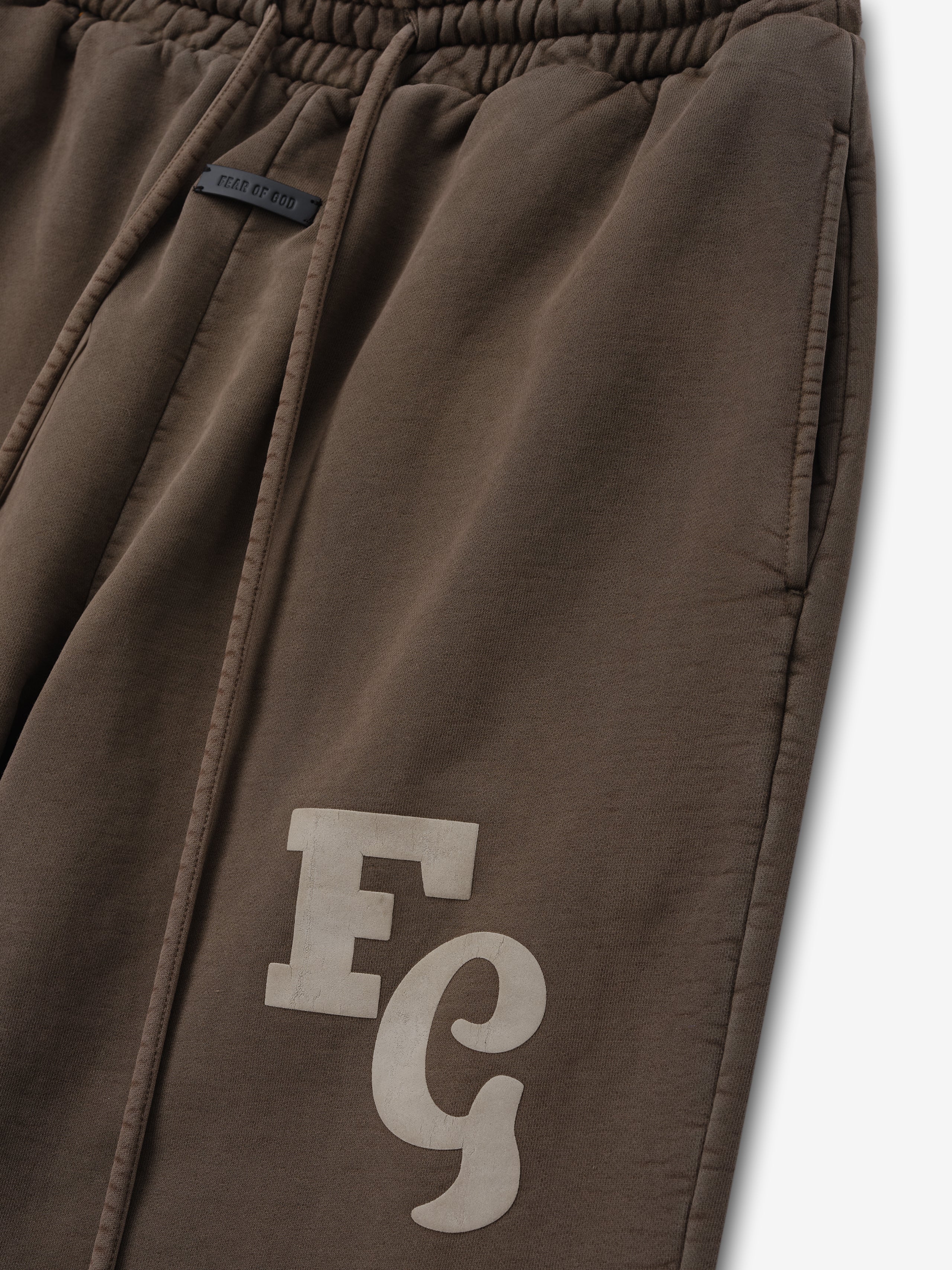 Close-up of faded brown sweatpants with elastic waistband, side pockets, drawstrings, and light "FG" logo on thigh