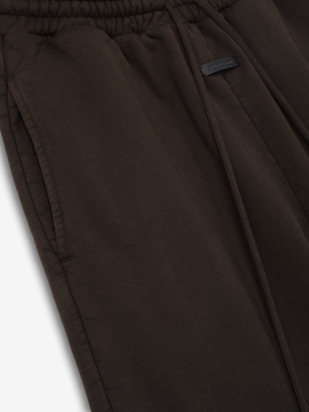 Dark brown sweatpants with elastic waistband, front drawstring, side pockets, and a small rectangular patch detail