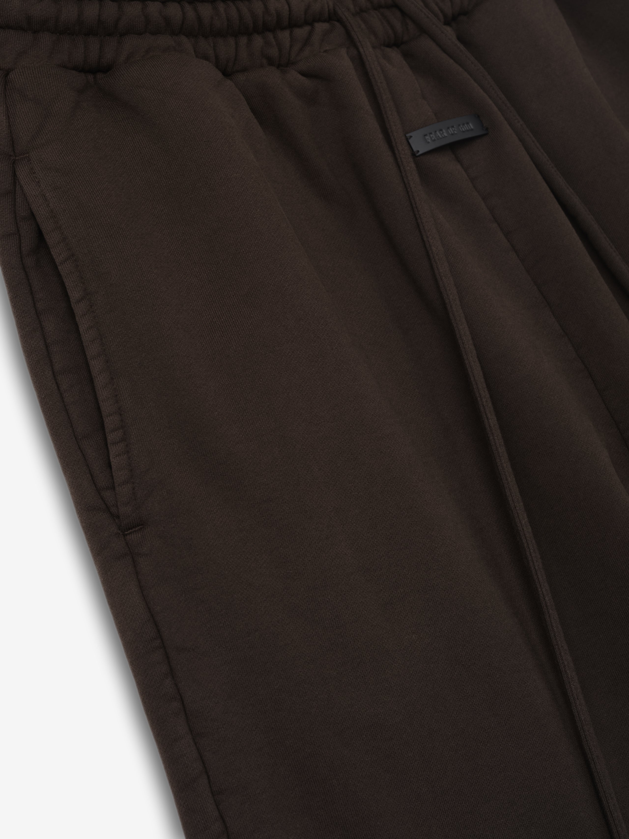 Dark brown sweatpants with elastic waistband, front drawstring, side pockets, and a small rectangular patch detail