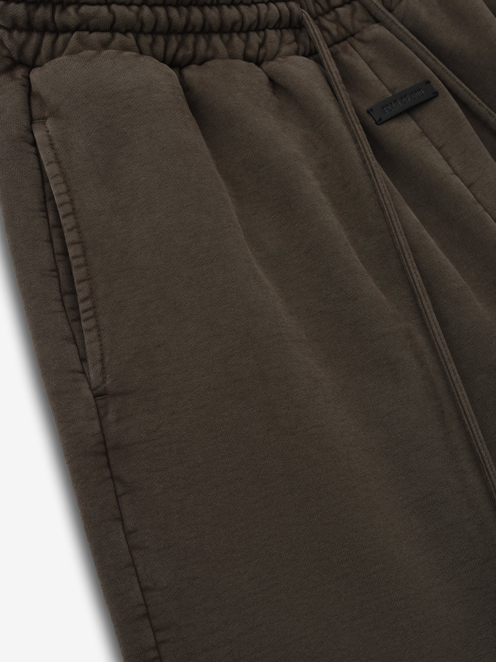 Close-up of dark olive green sweatpants with elastic waistband, side pocket, and subtle fabric tag on a white background