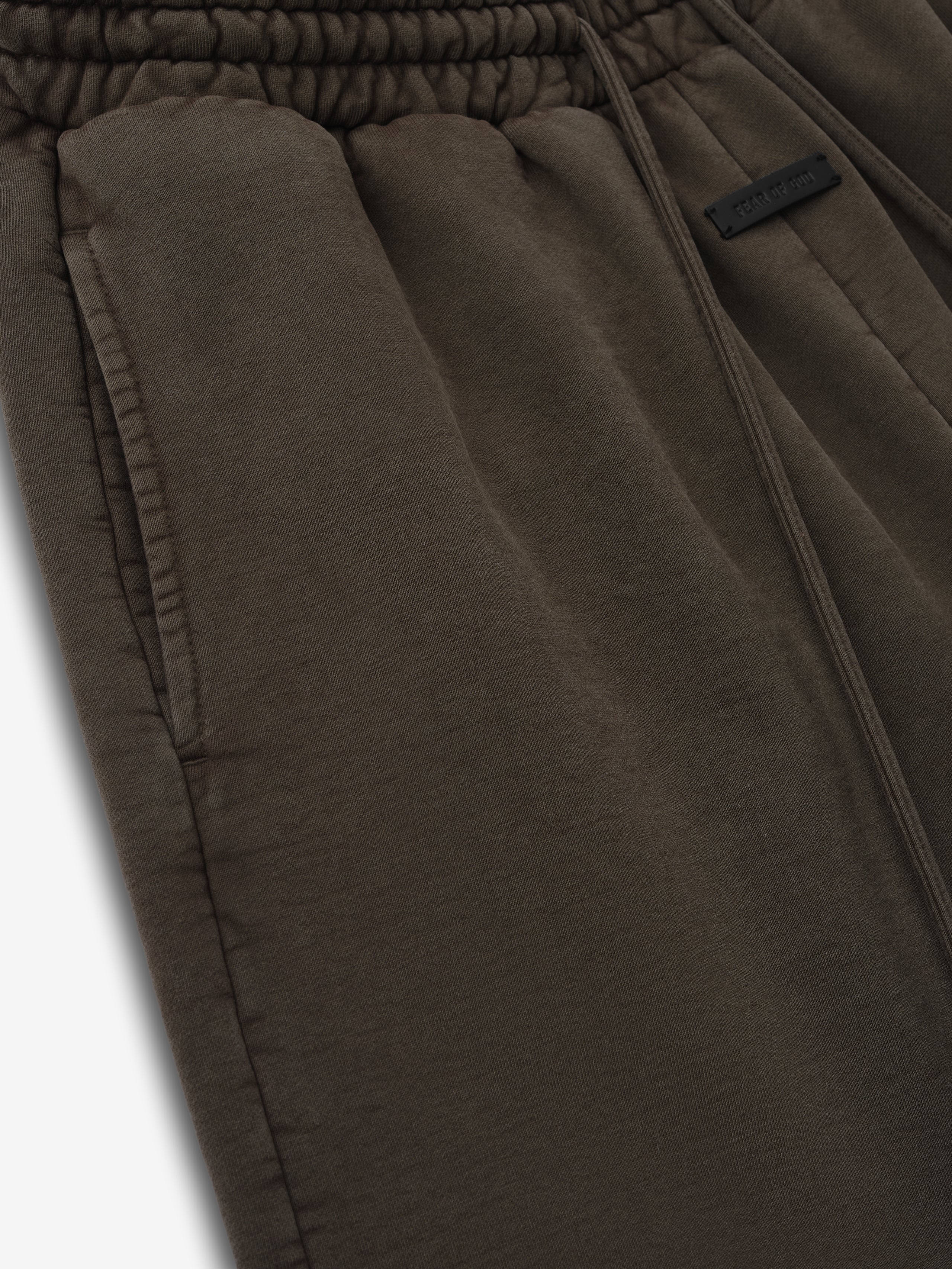 Close-up of dark olive green sweatpants with elastic waistband, side pocket, and subtle fabric tag on a white background