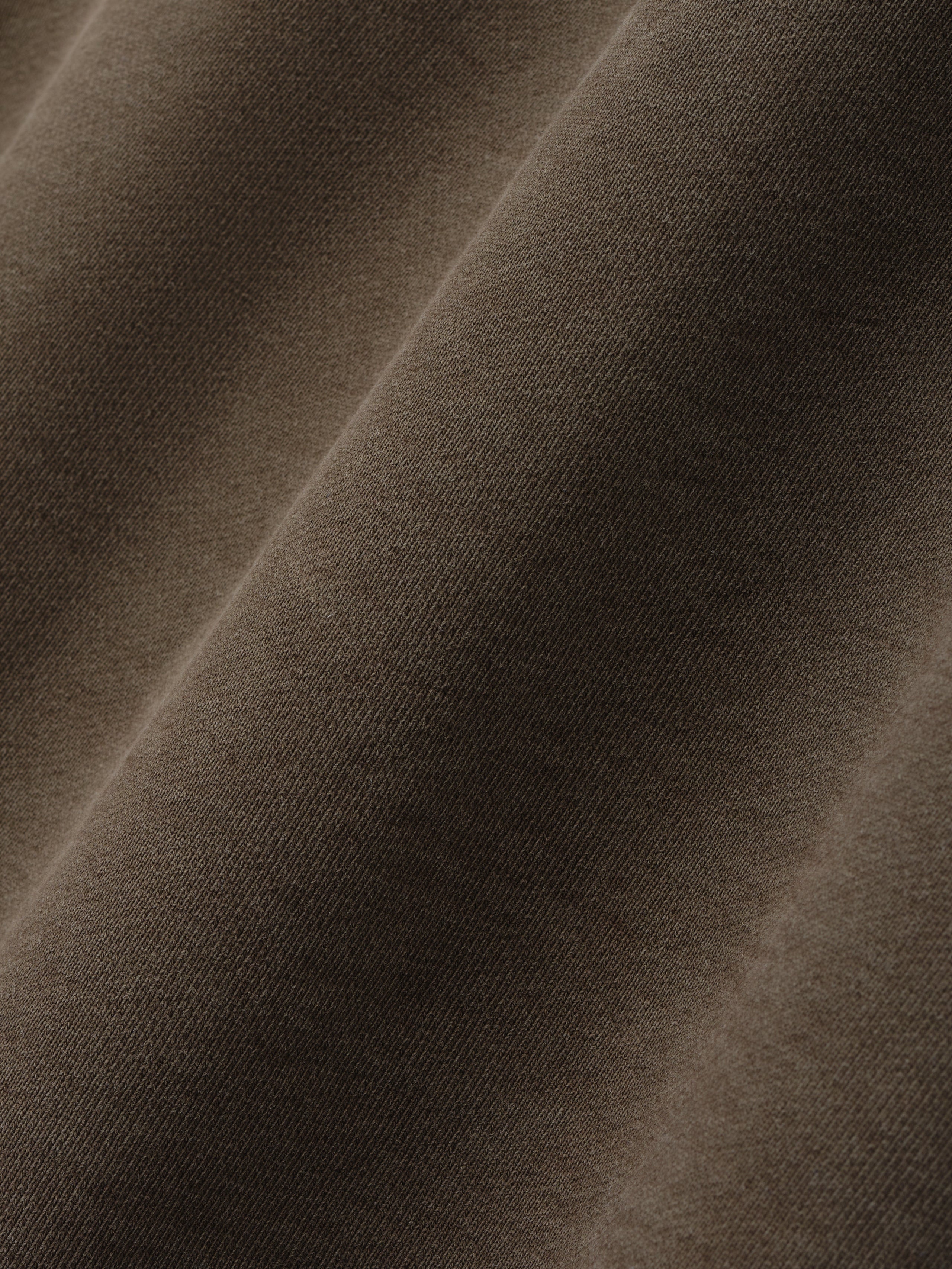 Close-up of smooth brown fabric texture with soft folds and fine knit detail on a neutral background