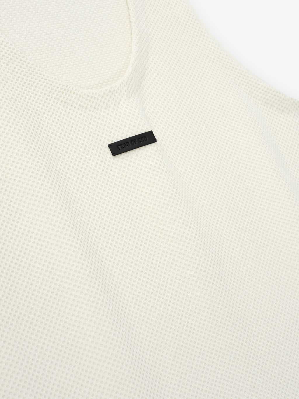 Close-up of off-white textured knit fabric with small black rectangular label stitched near neckline