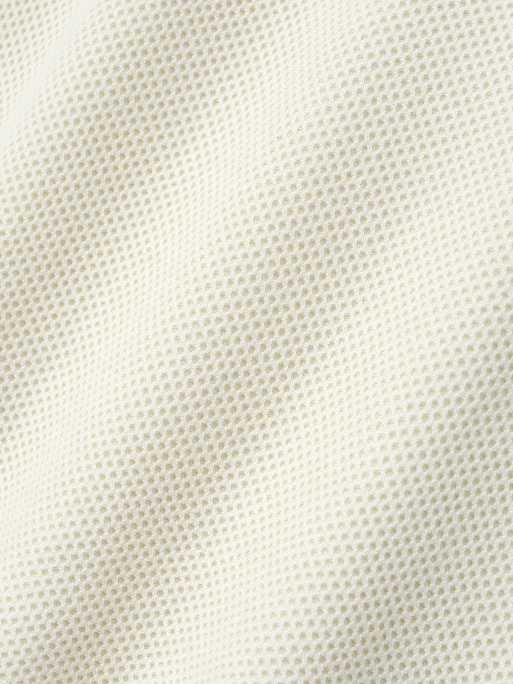 Close-up of off-white waffle knit fabric showing textured pattern with soft folds and subtle shadows