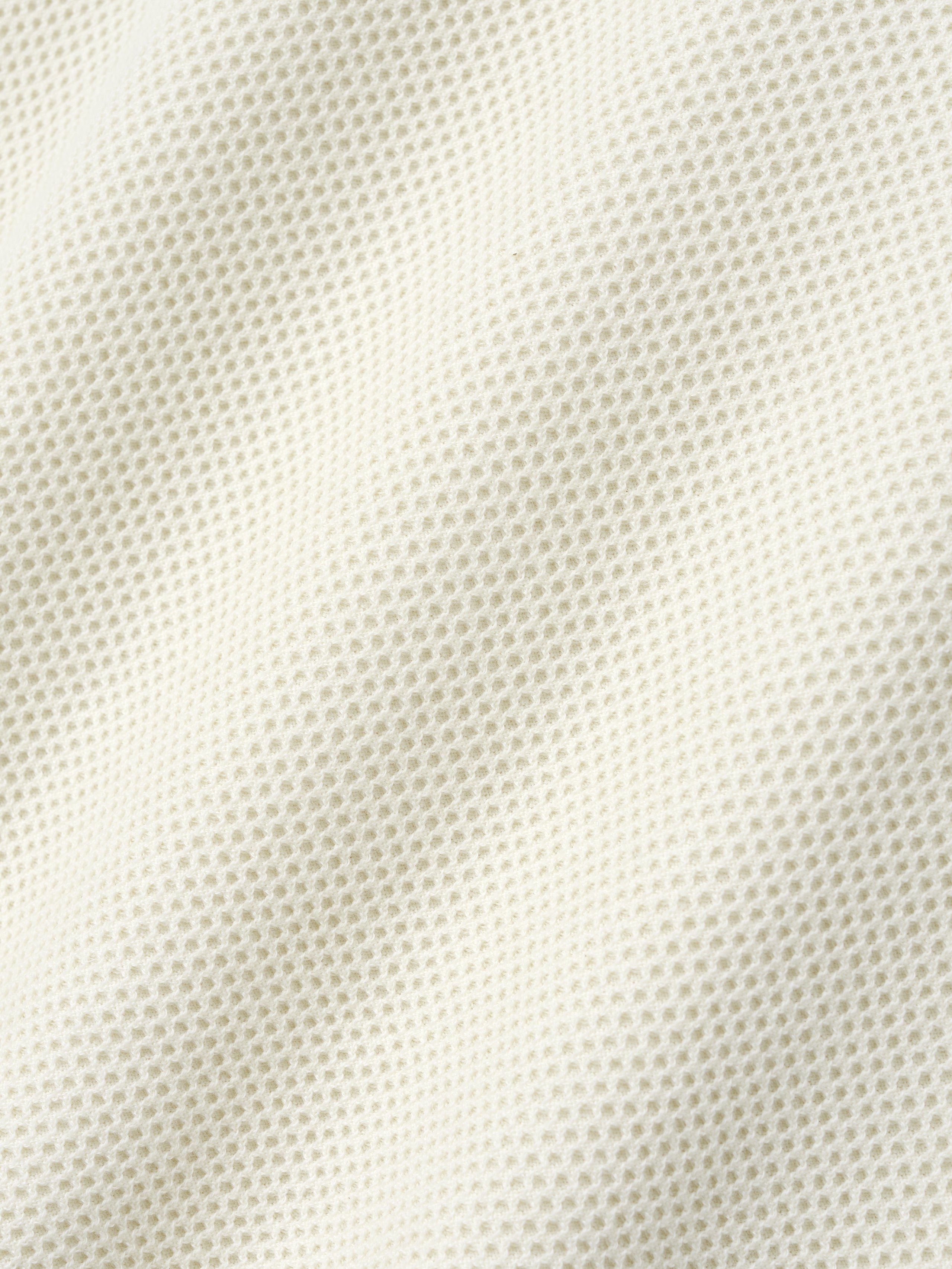 Close-up of off-white waffle knit fabric showing textured pattern with soft folds and subtle shadows