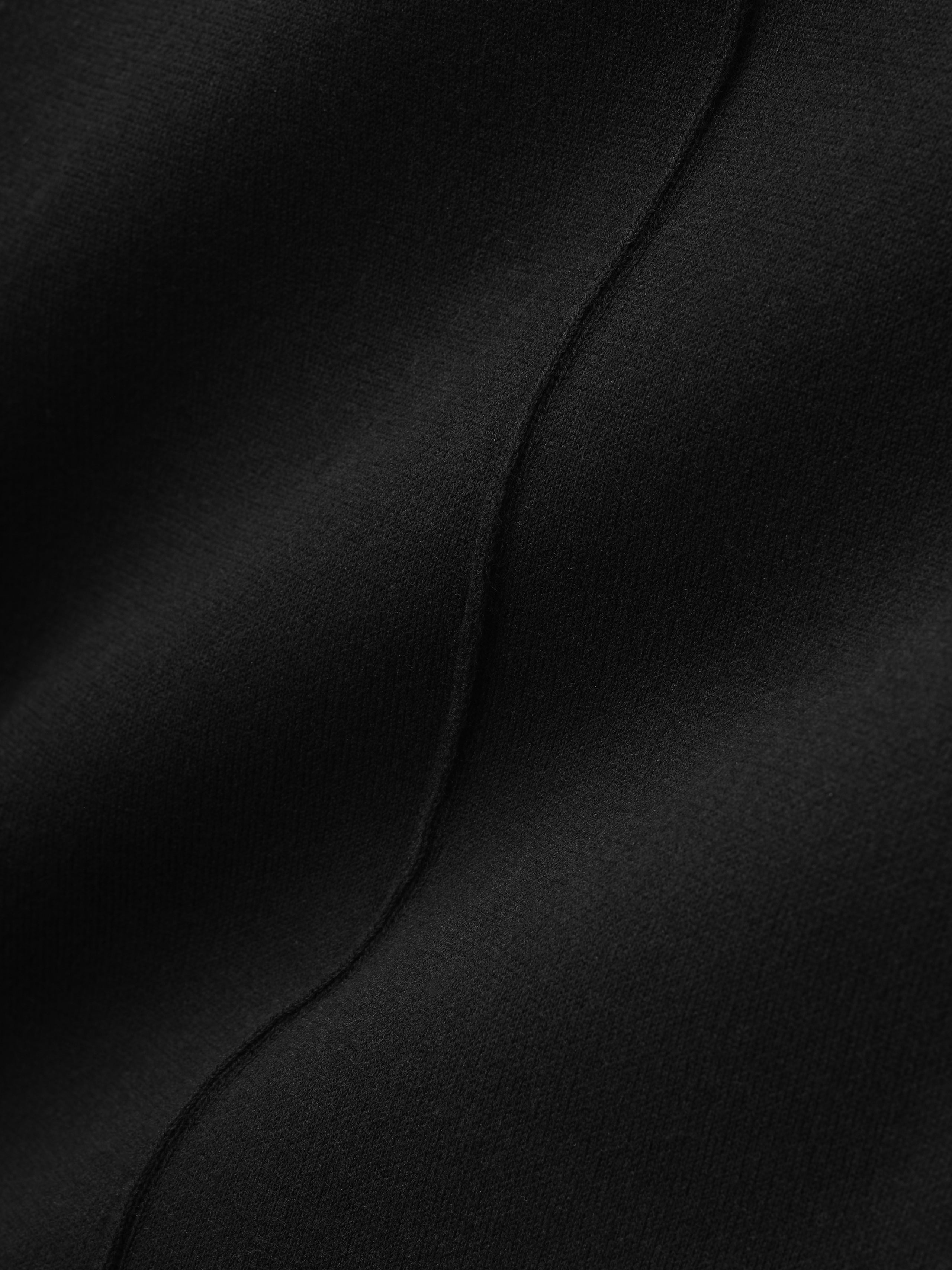 close-up detail of black double-knit cotton-nylon fabric showing smooth seam texture on flared jogging pants