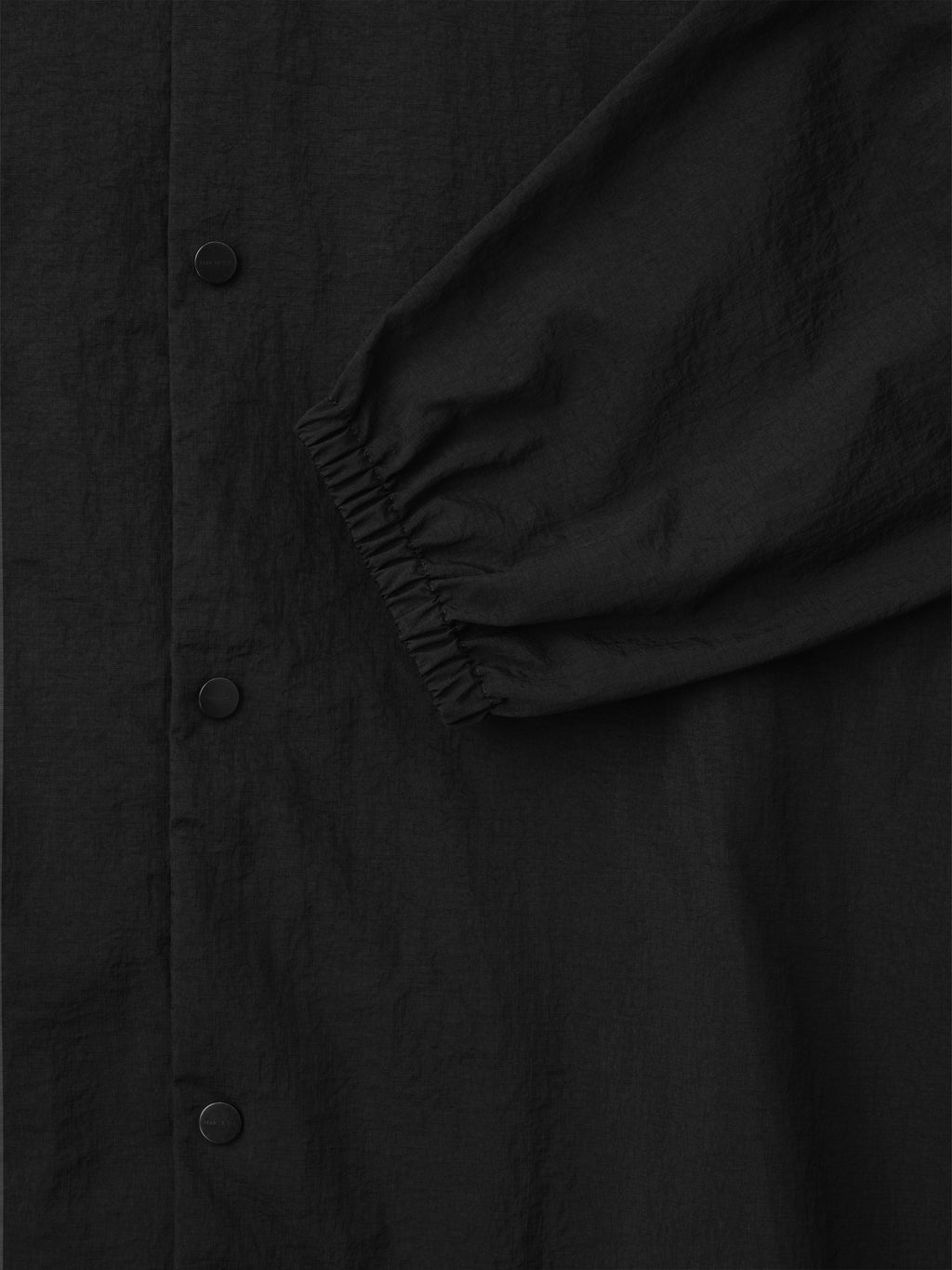 black recycled nylon ripstop fabric close-up showing matte snap buttons and elasticated cuff detail on sleeve