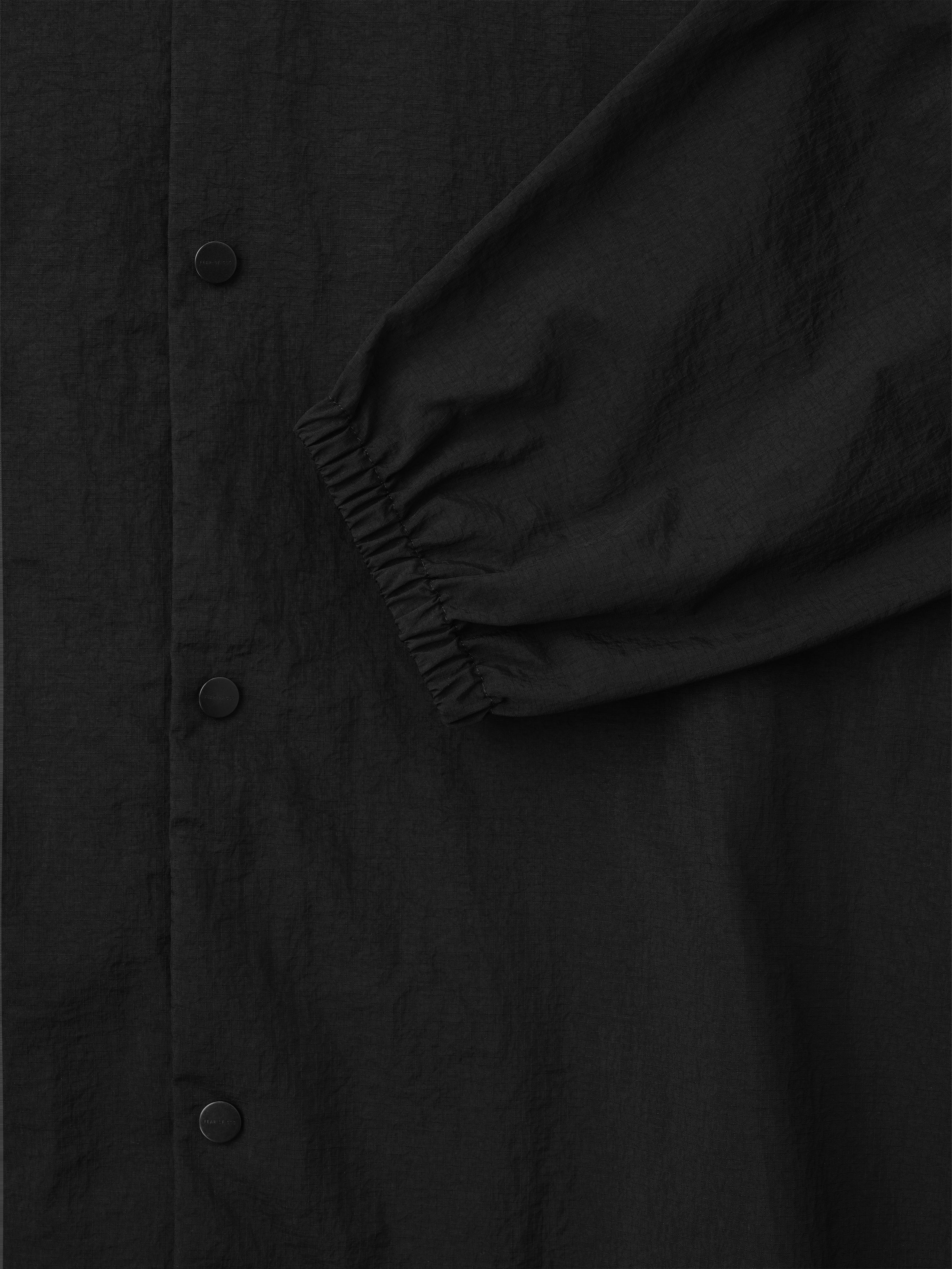 black recycled nylon ripstop fabric close-up showing matte snap buttons and elasticated cuff detail on sleeve