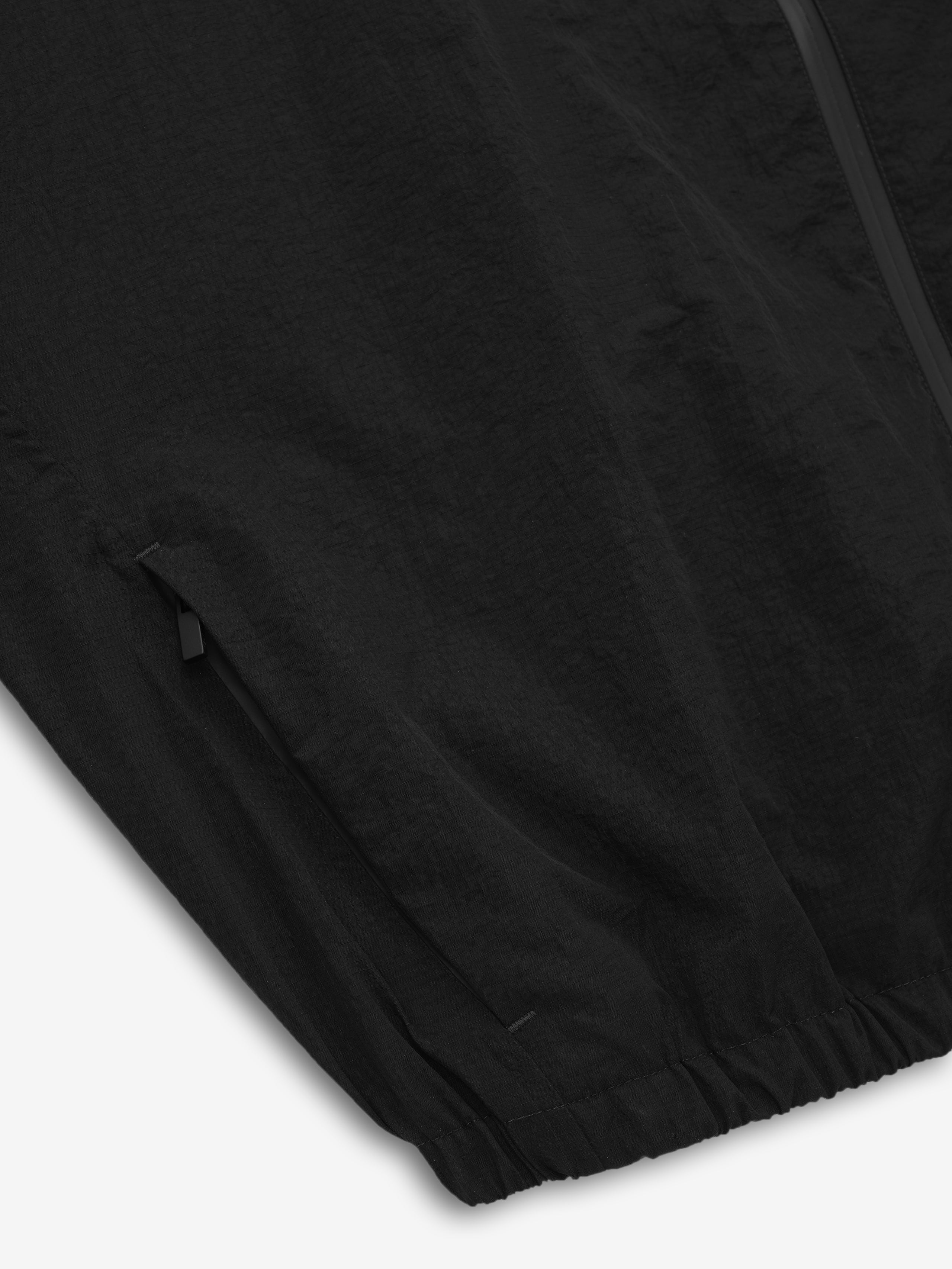 close-up of black recycled nylon ripstop fabric with zippered pocket and elasticated hem detail on jacket