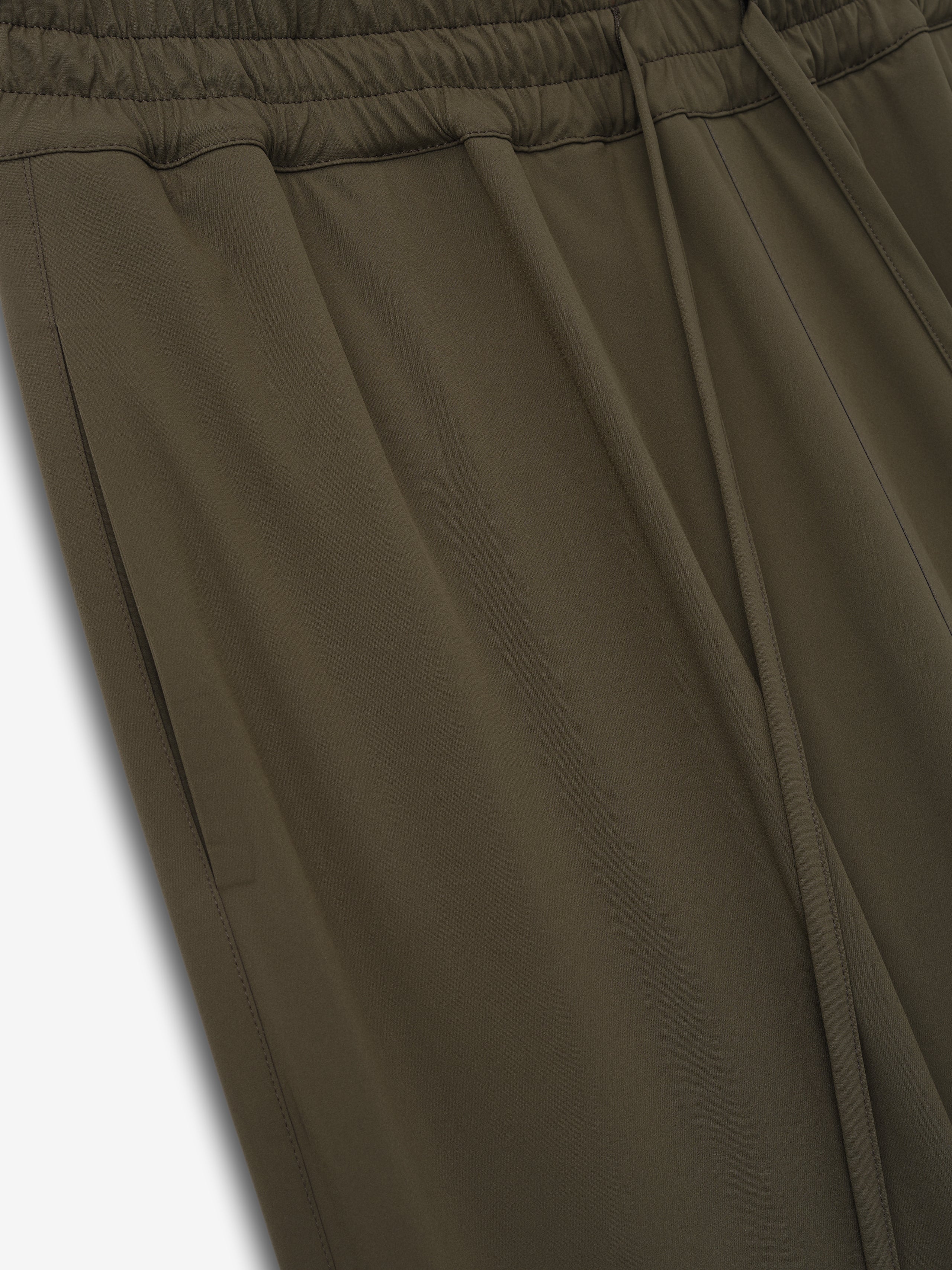 Close-up of olive green pants showing elastic waistband, side pockets, and smooth fabric texture on a light background