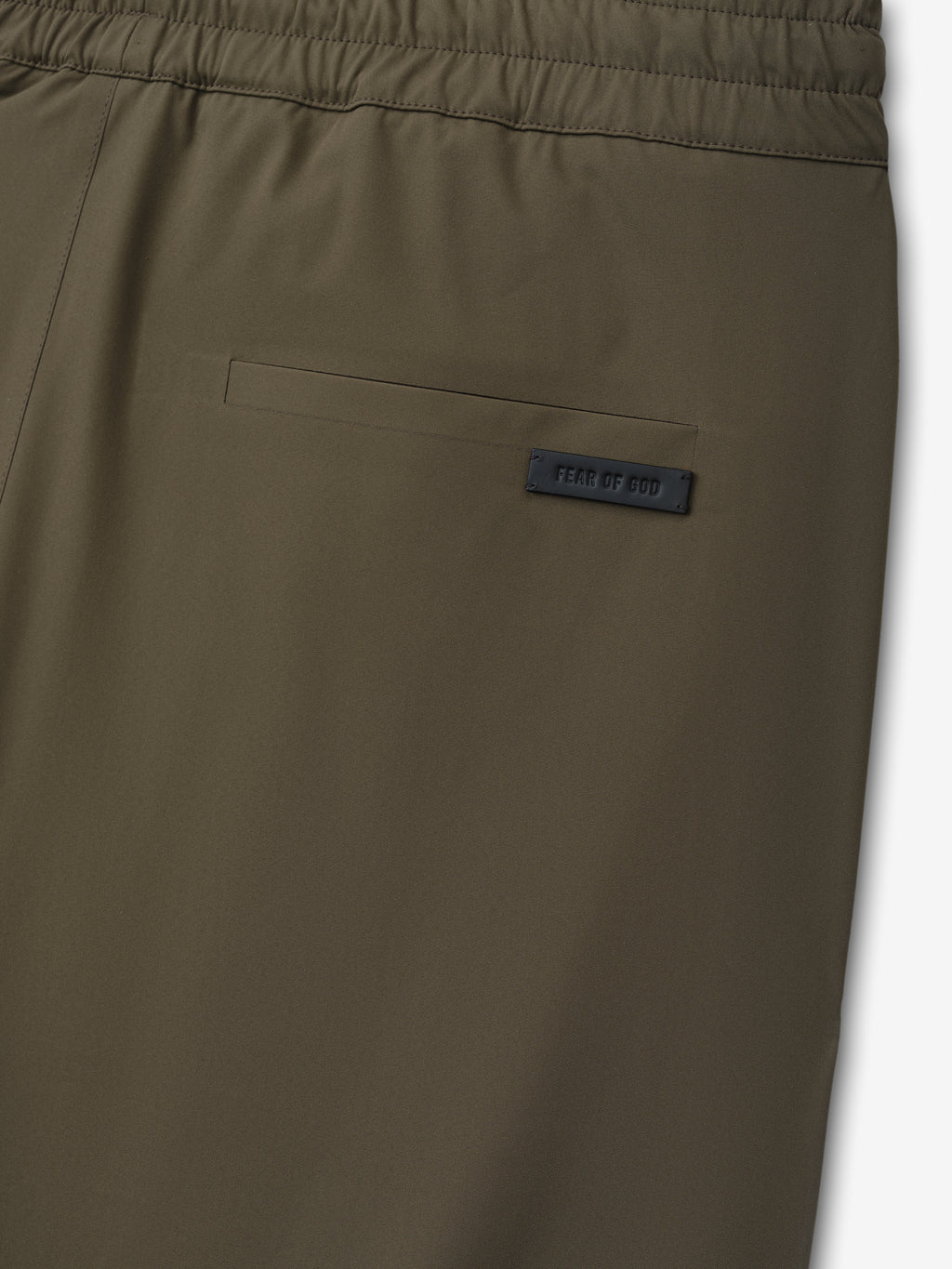 Close-up of olive green fabric with back pocket and small black rectangular label stitched near pocket edge