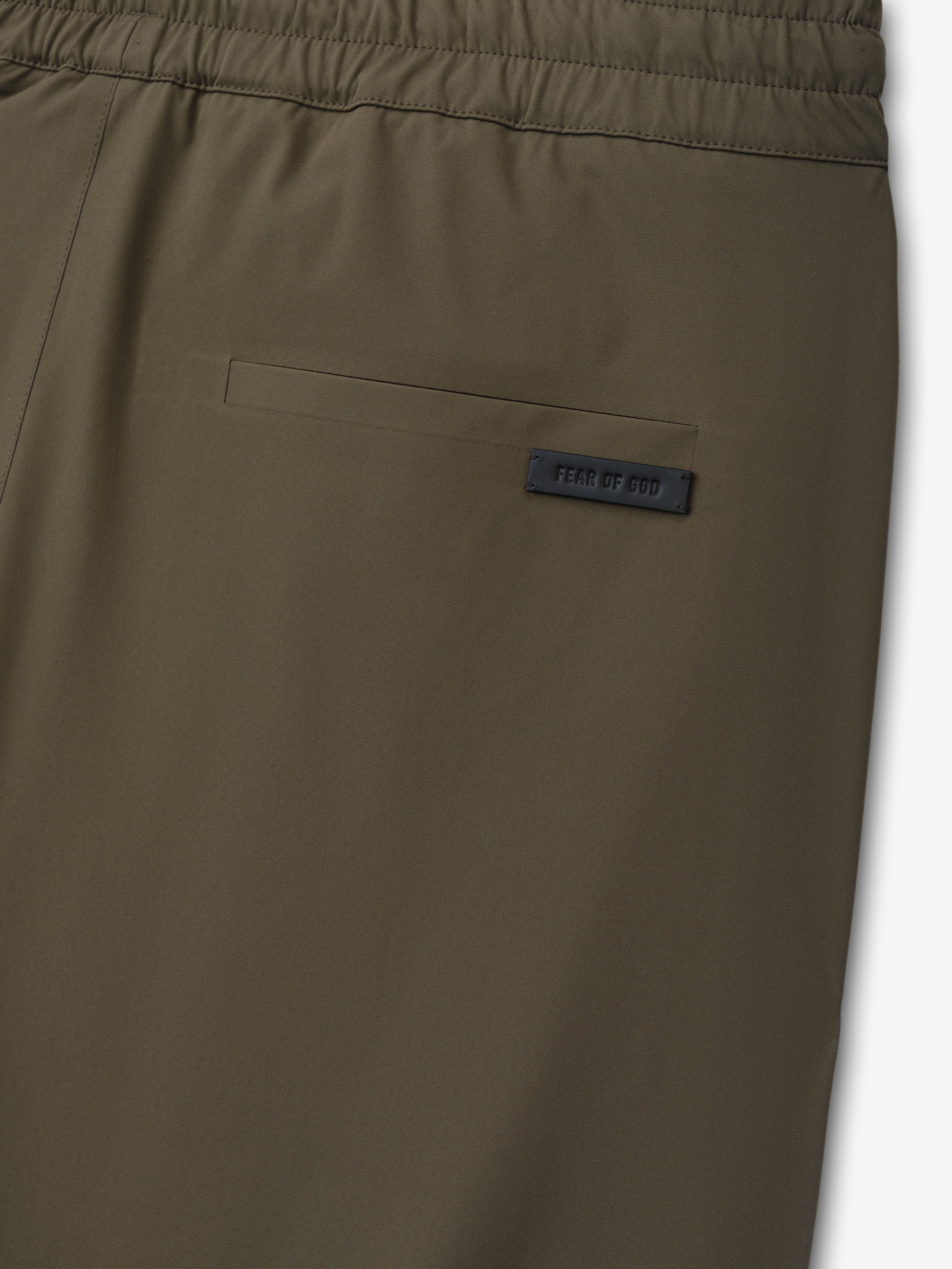 Close-up of olive green fabric with back pocket and small black rectangular label stitched near pocket edge