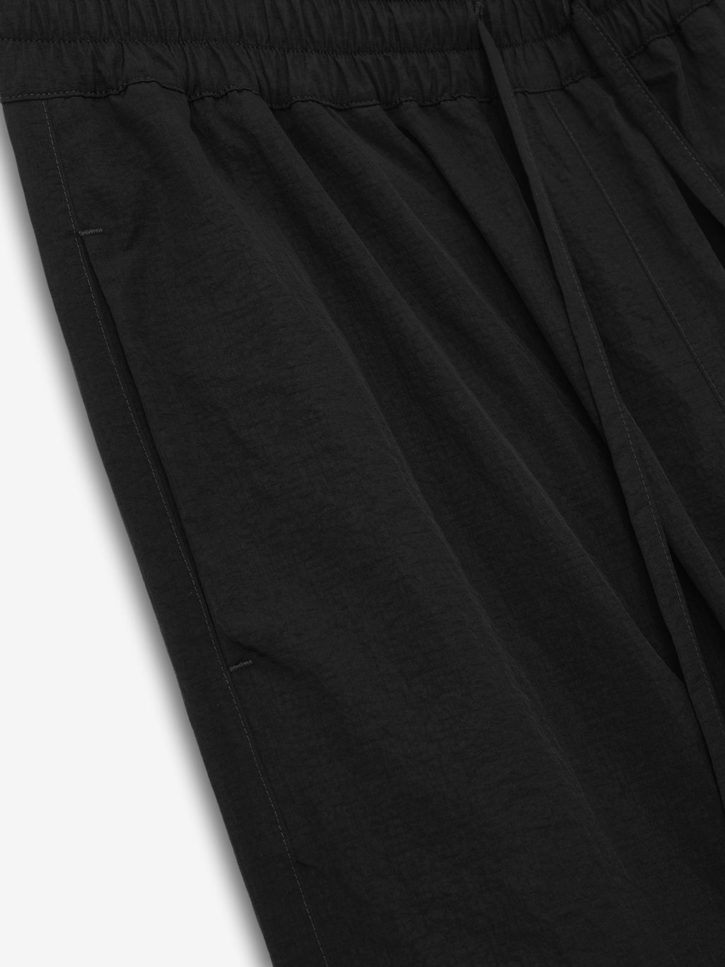 close-up of black recycled nylon ripstop fabric with elastic waistband and side pocket detail on tech track pants