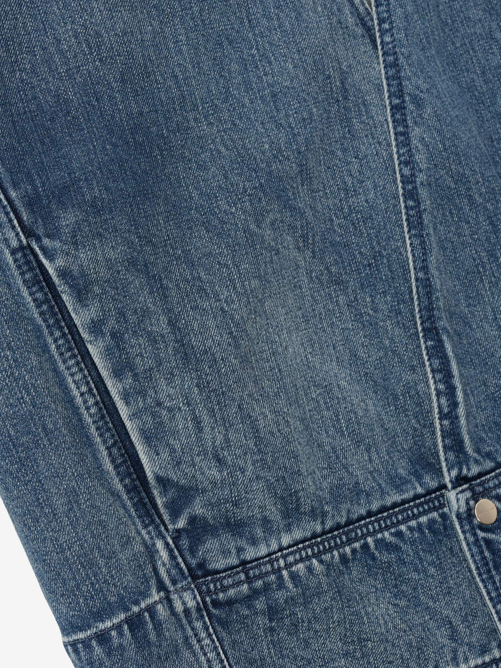 close-up of blue indigo denim fabric with detailed stitching and metal rivet on lapelless jacket panel