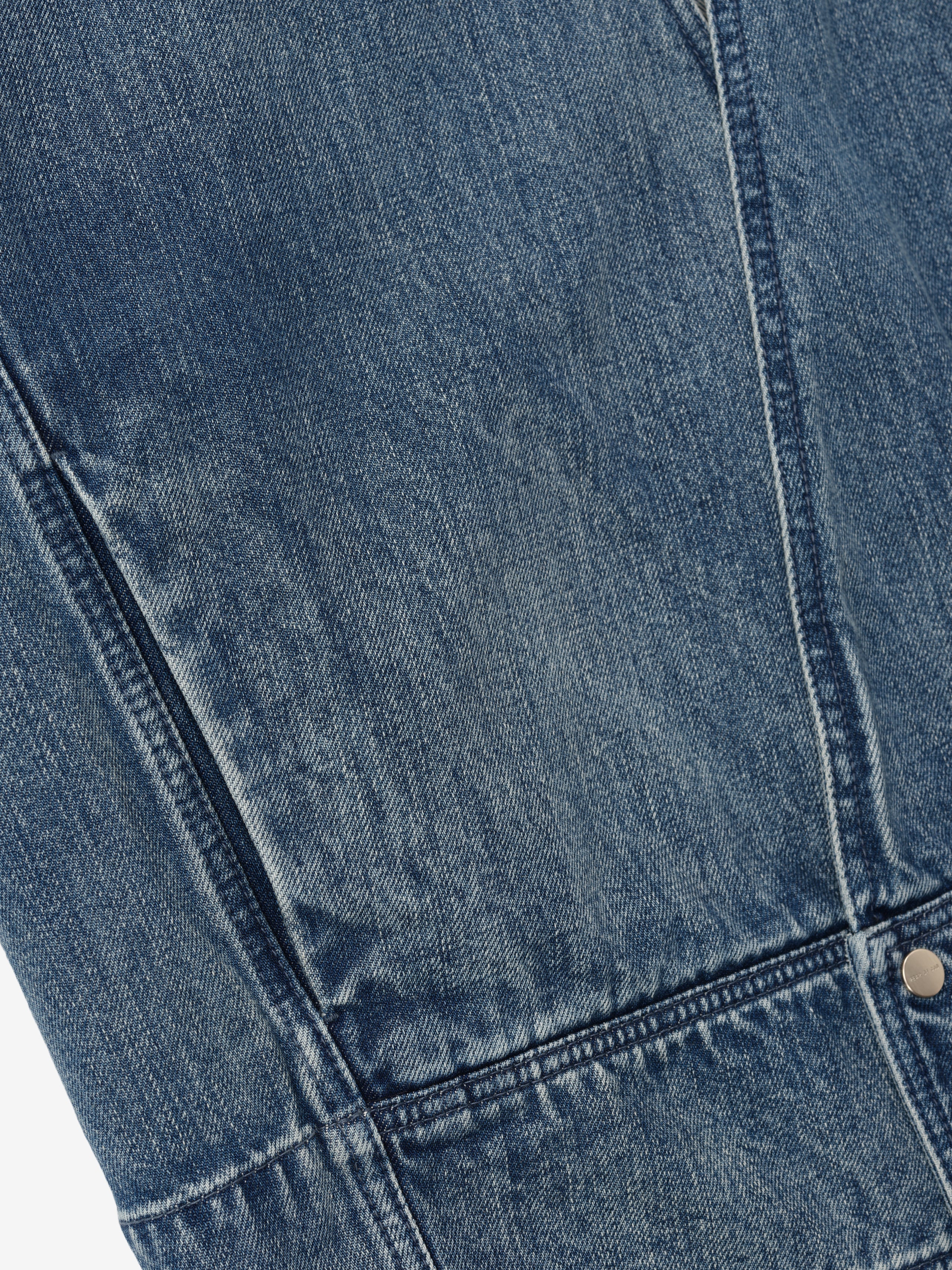 close-up of blue indigo denim fabric with detailed stitching and metal rivet on lapelless jacket panel